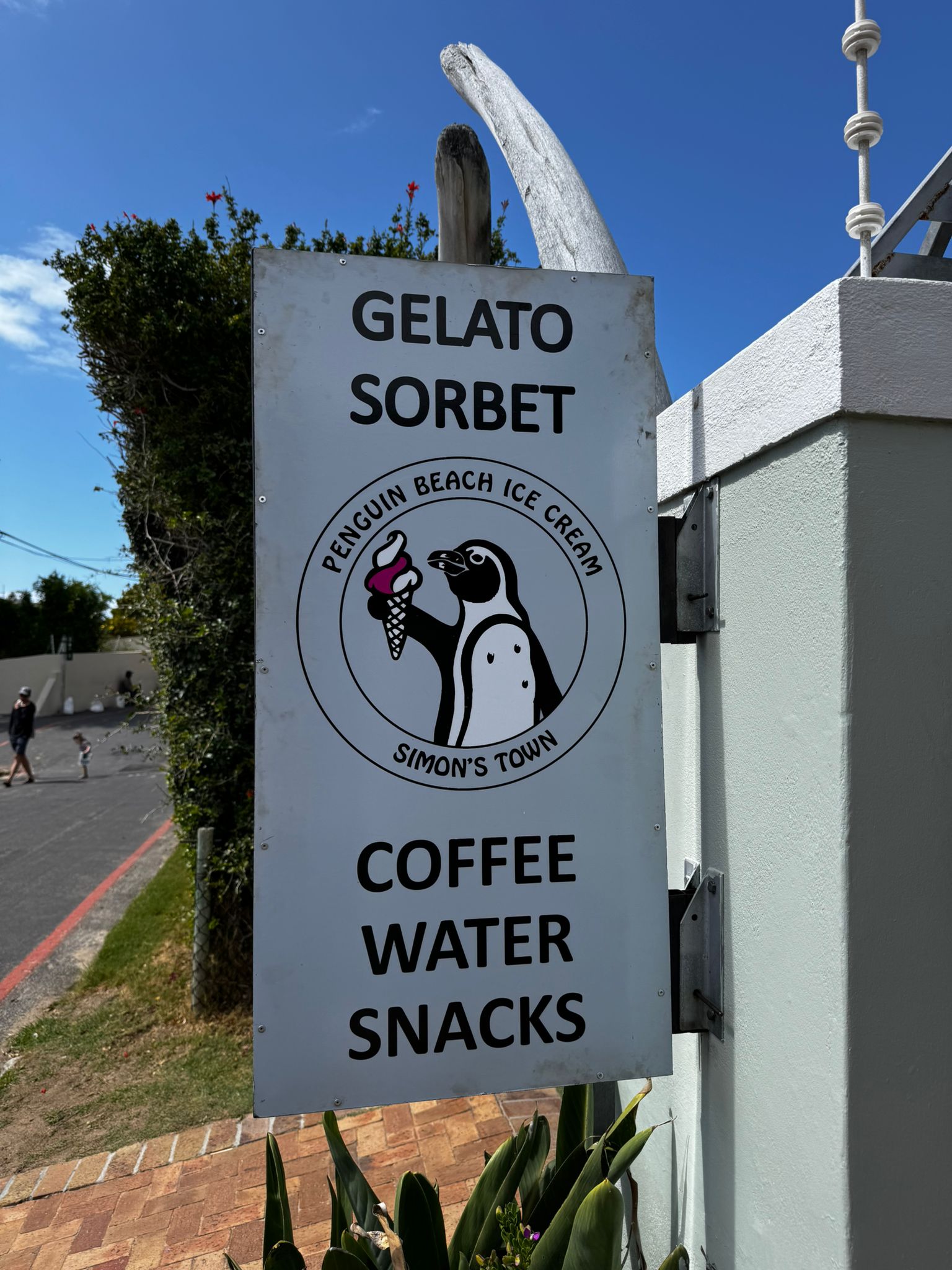 A sign on a wall for Gelato Sorbet with a drawing of a penguin holding up an ice cream cone. The sign says "Penguin Beach Ice Cream, Simon's Town".