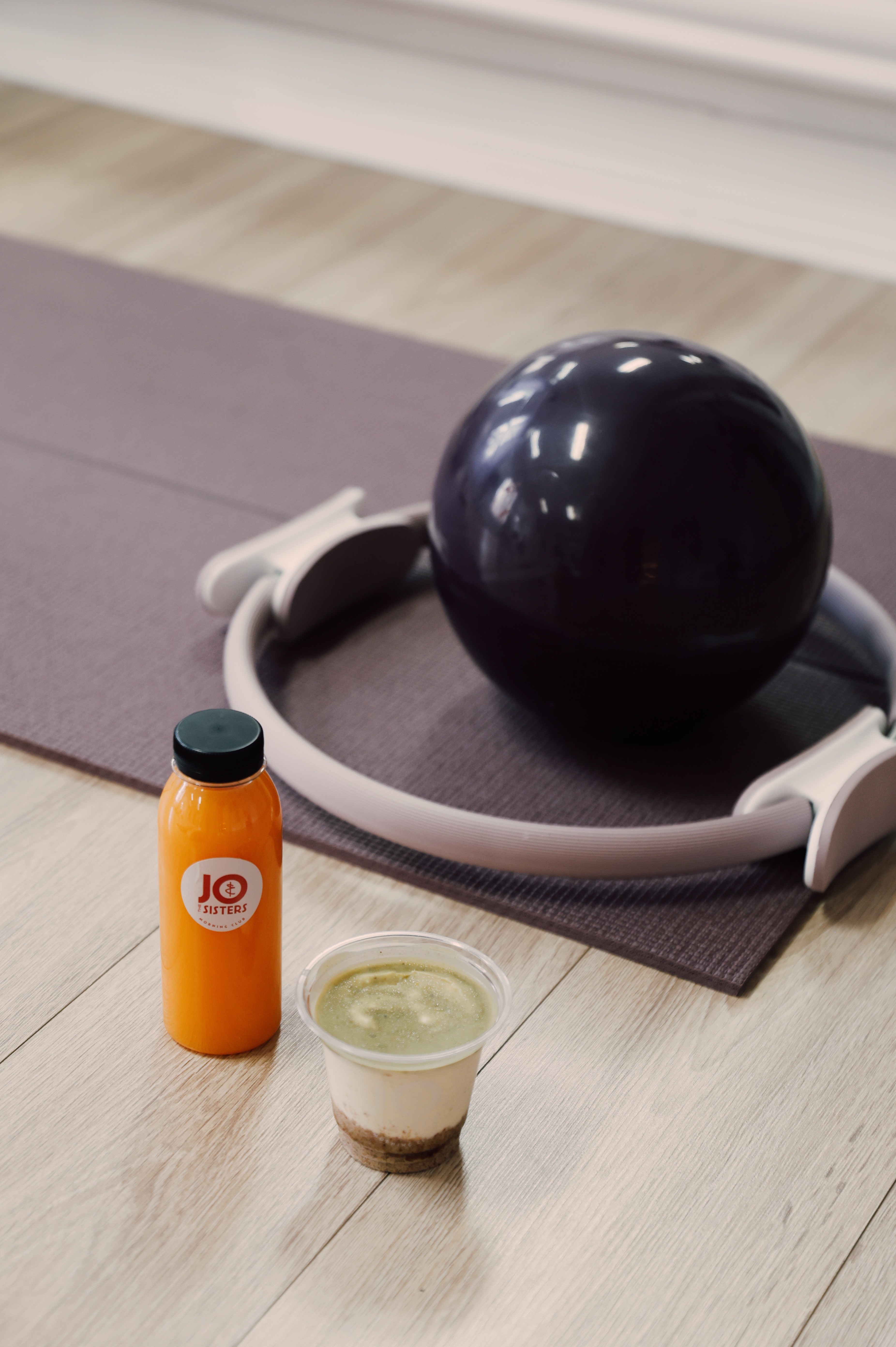 Fresh orange juice and a matcha dessert placed on the floor next to Pilates equipment at a reformer studio.