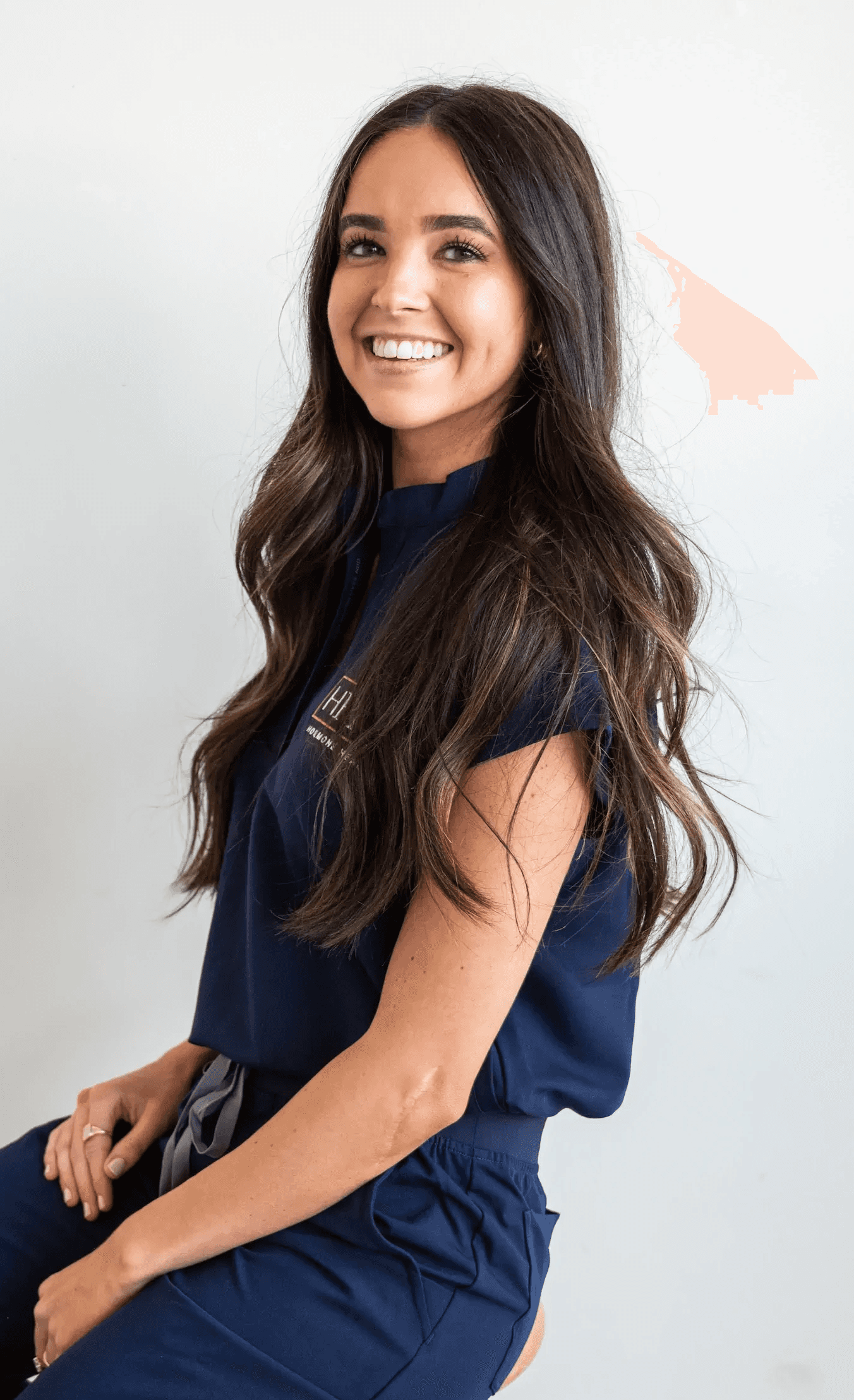 Portrait of Jamie Ruiz, a certified Physician Associate, smiling in a professional medical setting with shelves of supplements and medical products in the background.
