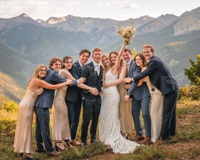 The couple celebrate in a group embrace as the bride raises her bouquet.