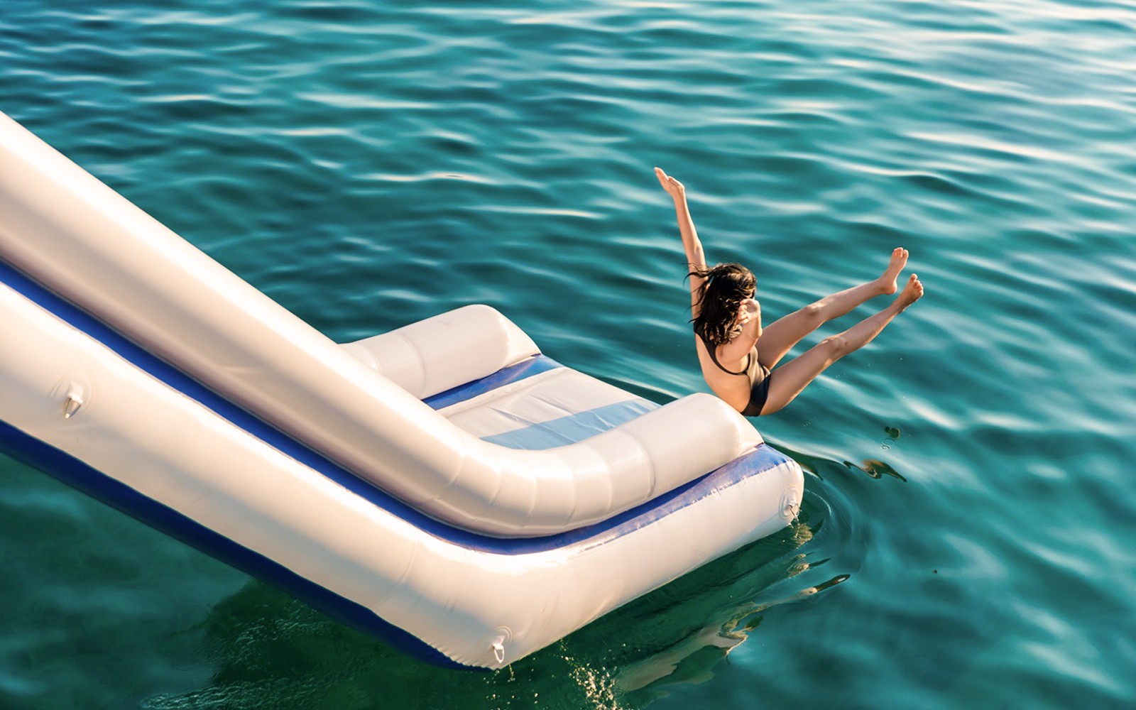 一个人从充气滑梯滑入翠绿色的水中，四周环绕着石灰岩山脉。