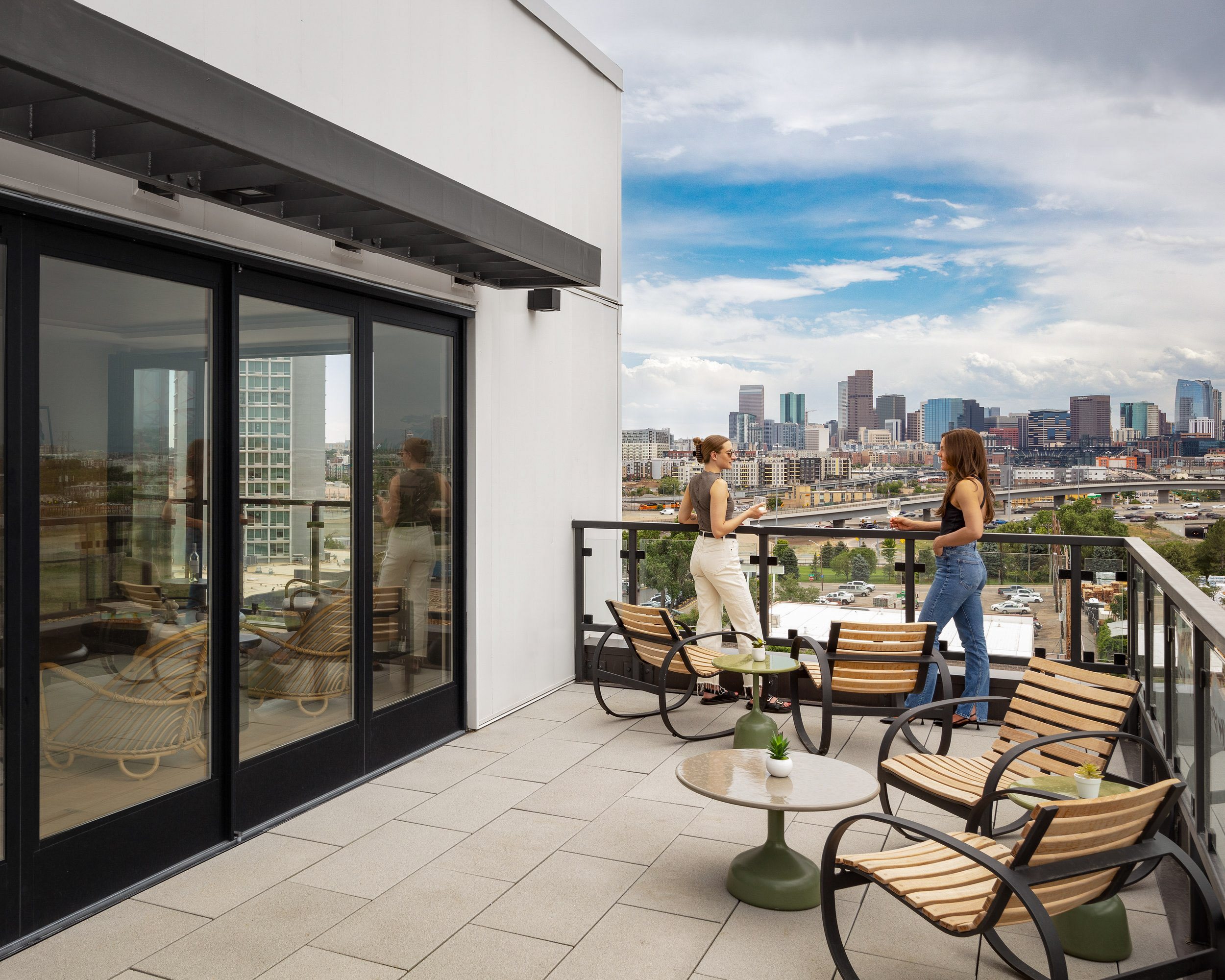 Two women on rooftop balcony overlooking cityscape.