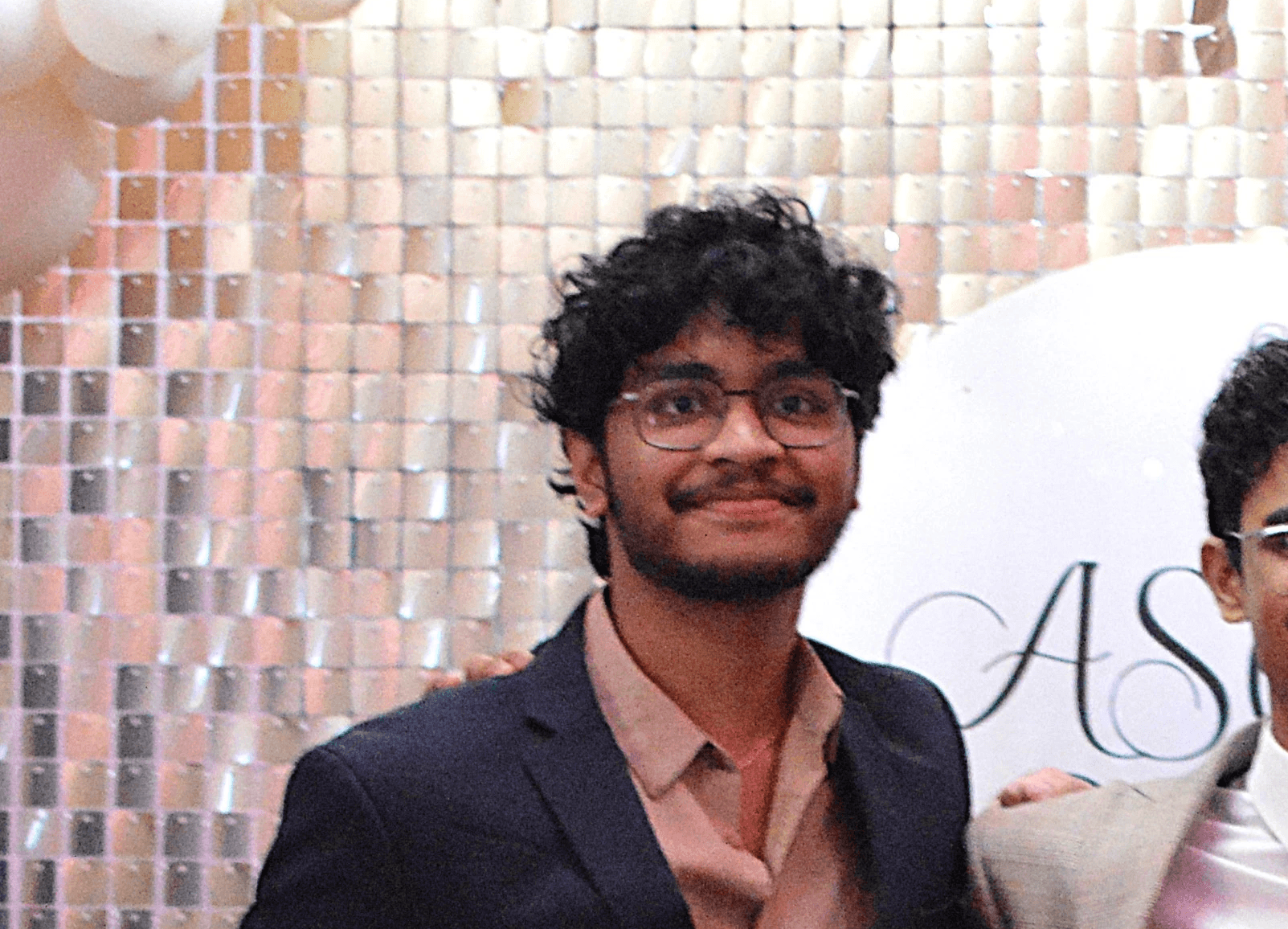 Woman in a stylish orange visor, yellow earrings, and a navy lace top against a blue backdrop. Her expression is poised, with bold red lipstick.
