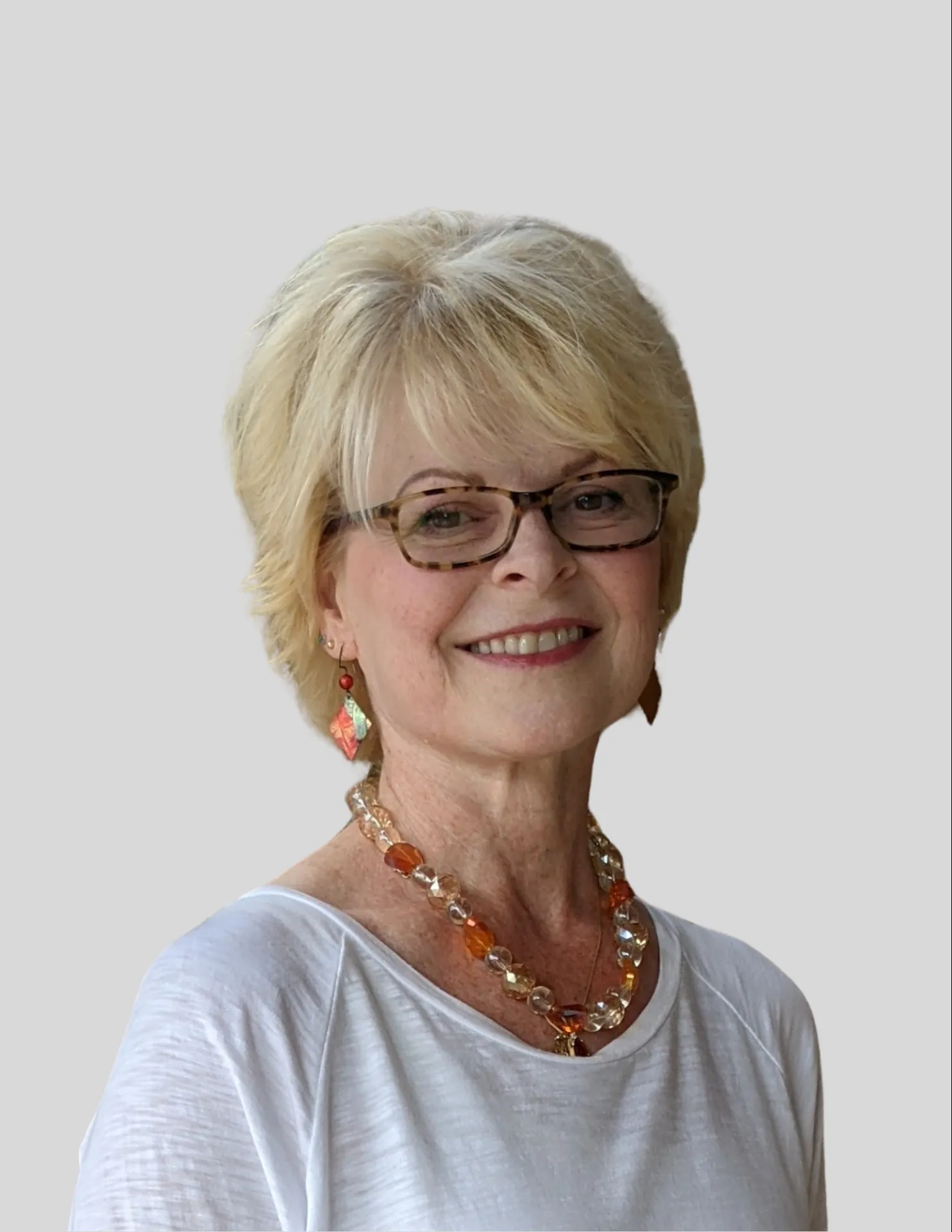 Senior woman with short blonde hair and glasses wearing an orange bead necklace.
