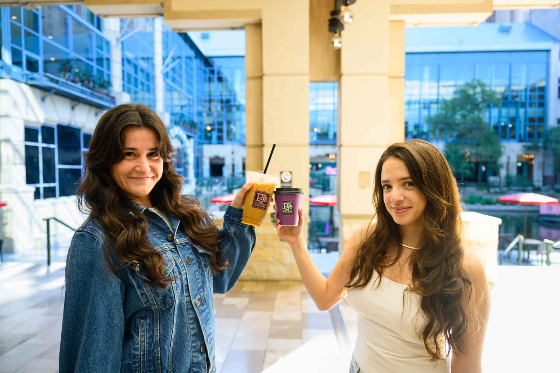 Two shoppers holding PJ’s Coffee drinks on a Rivercenter balcony overlooking the River Walk