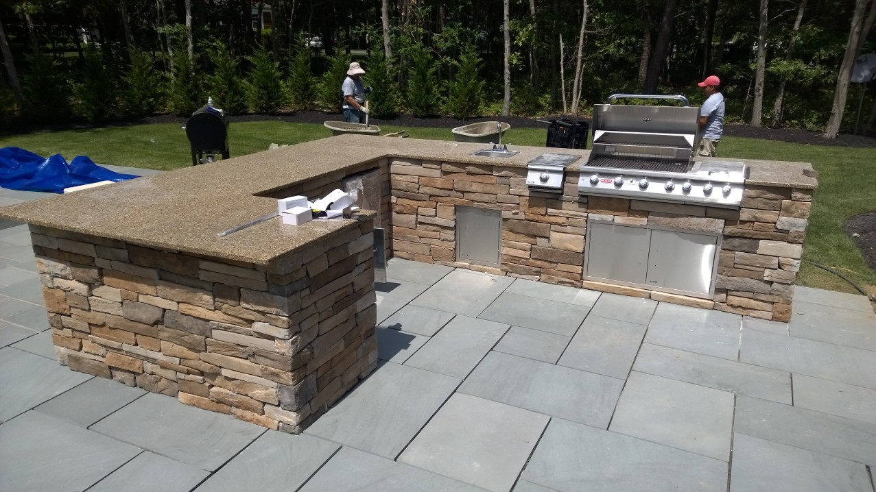 L-shaped outdoor bar and grill island built with tan ledgestone