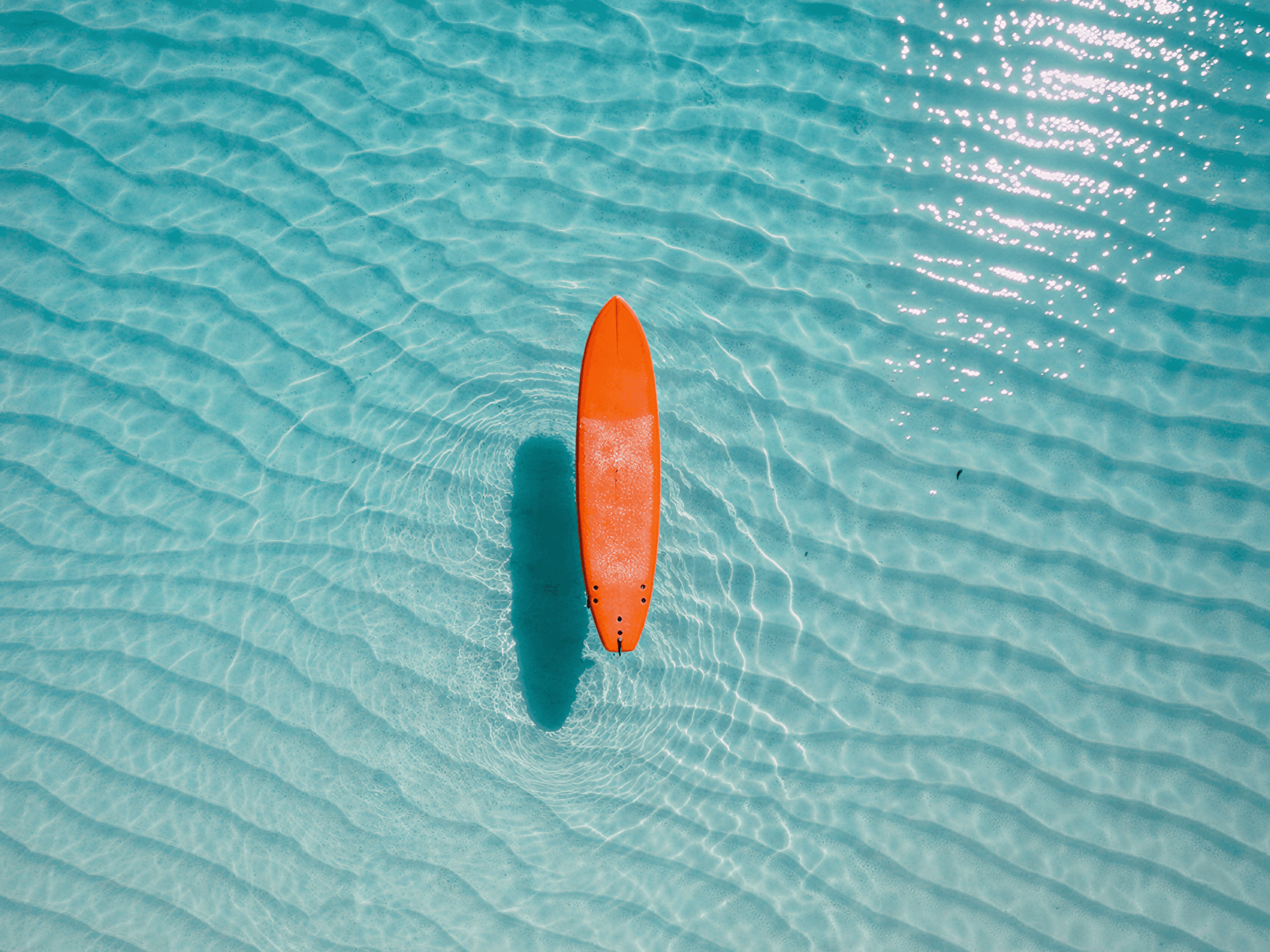 orange surfboard floating on clear turquoise water with sunlight reflections