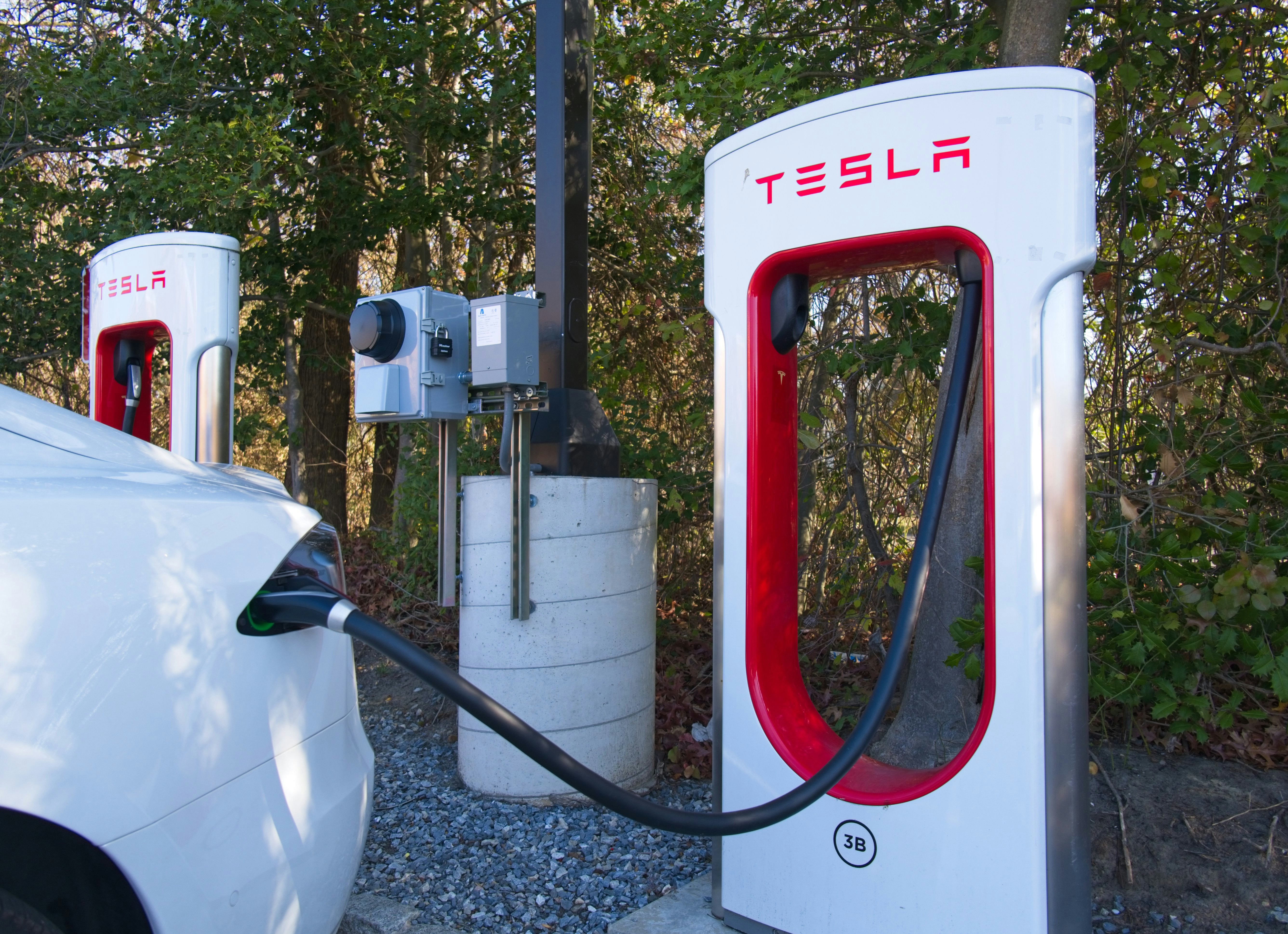 Tesla Supercharger station with a white electric vehicle plugged in, representing public EV charging infrastructure and the lithium-ion fire risk AF31-EV addresses