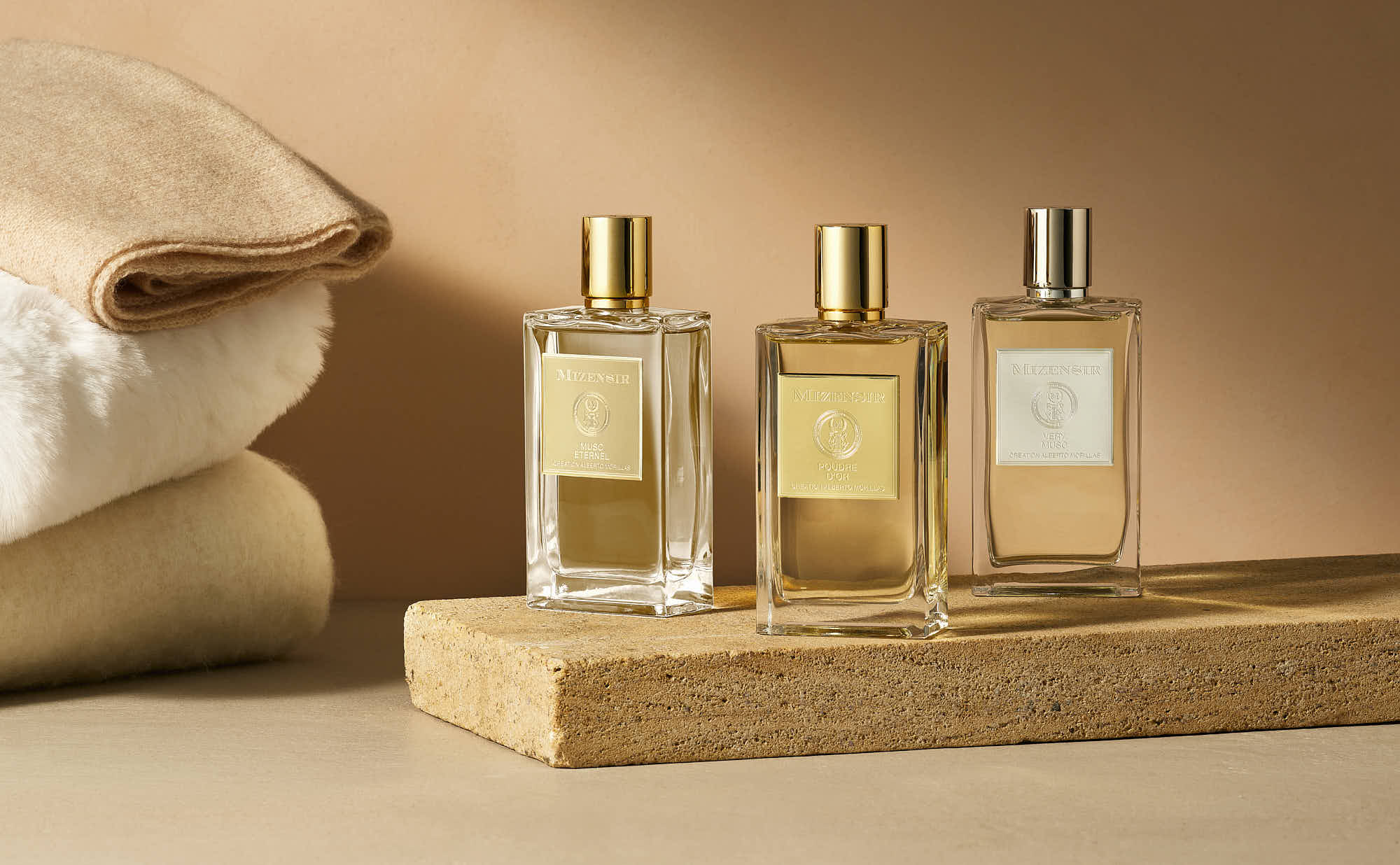 Three elegant perfume bottles displayed on a wooden surface, next to soft towels against a warm beige background.