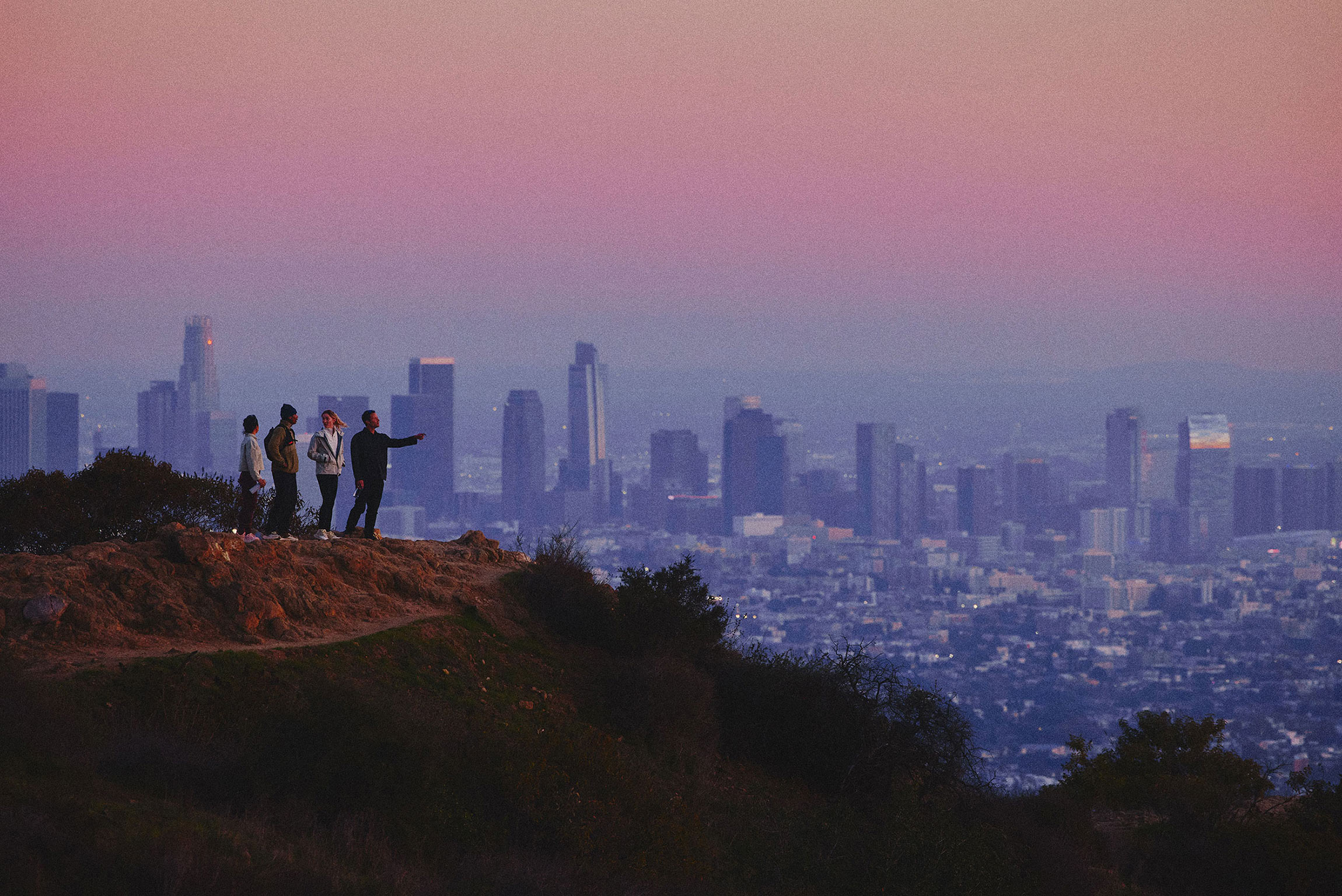 people standing off a clif looking over a city at sundown