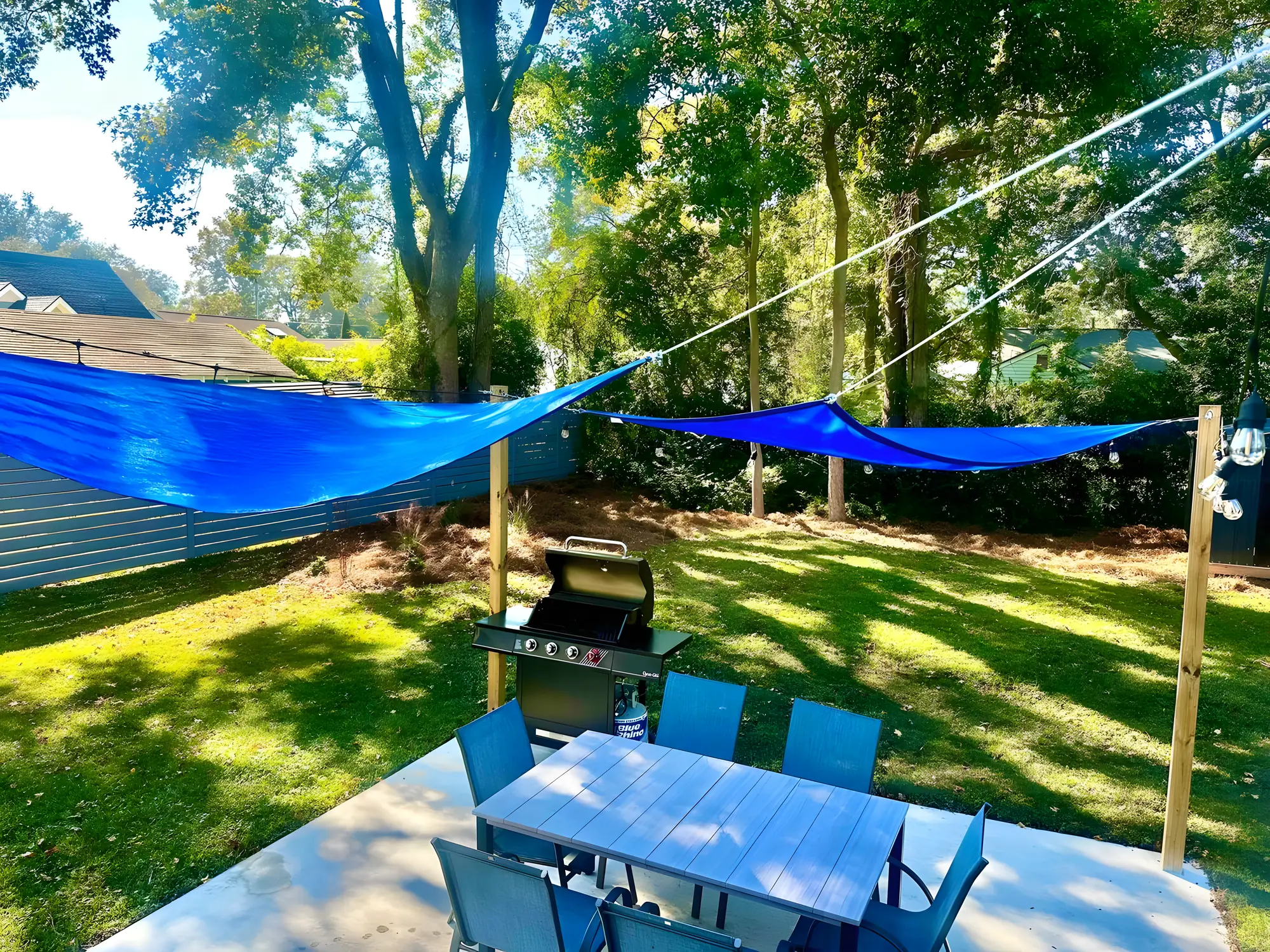Fenced backyard with a blue sail shade over the patio table and gas grill