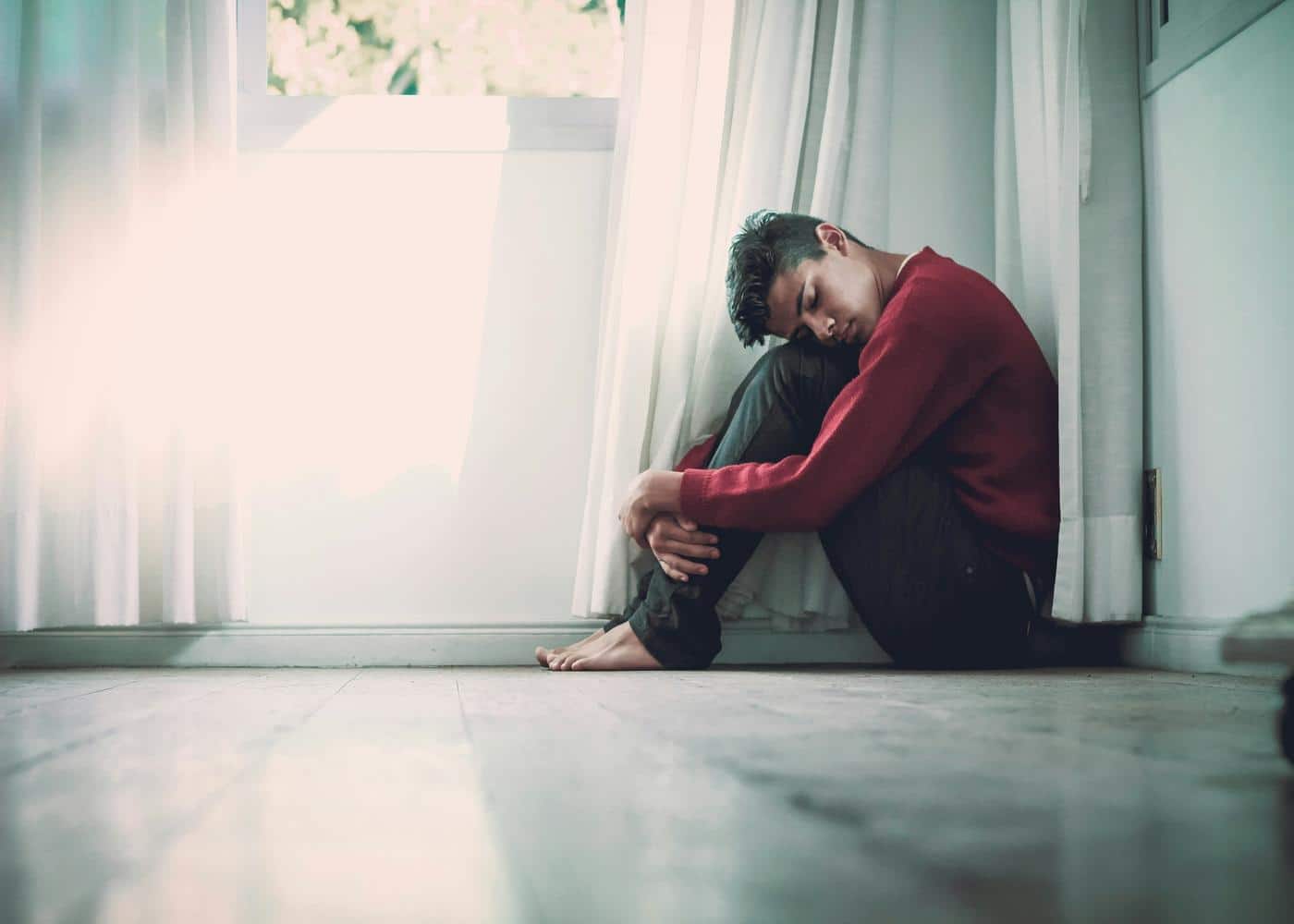 Health anxiety symptoms - Man sitting on the floor and holding his knees