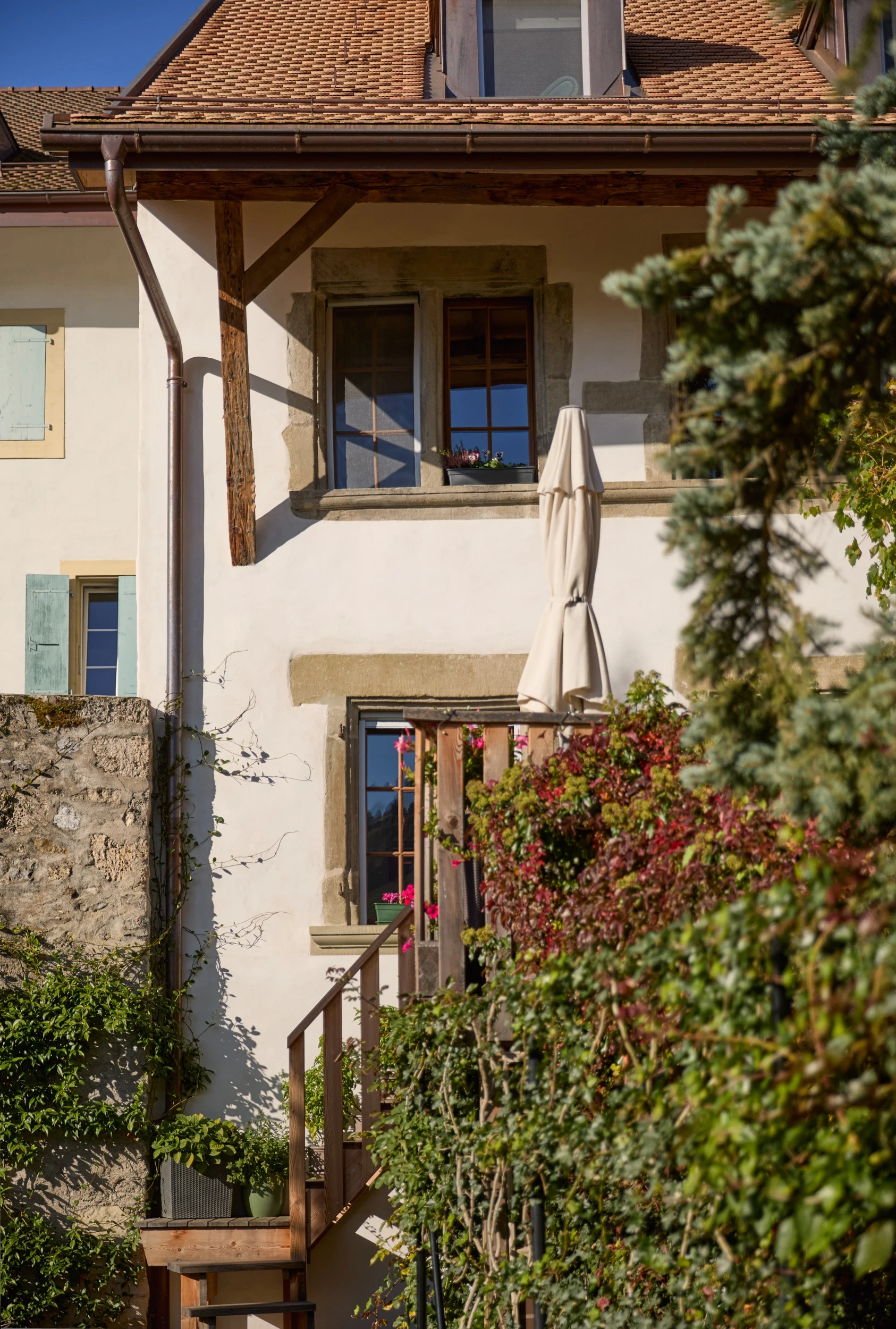 Façade côté jardin de la maison Muriset à Cully, avec ses six encadrements de fenêtres gothiques, sa terrasse en bois surélevée et son intégration harmonieuse dans le paysage du Lavaux. 