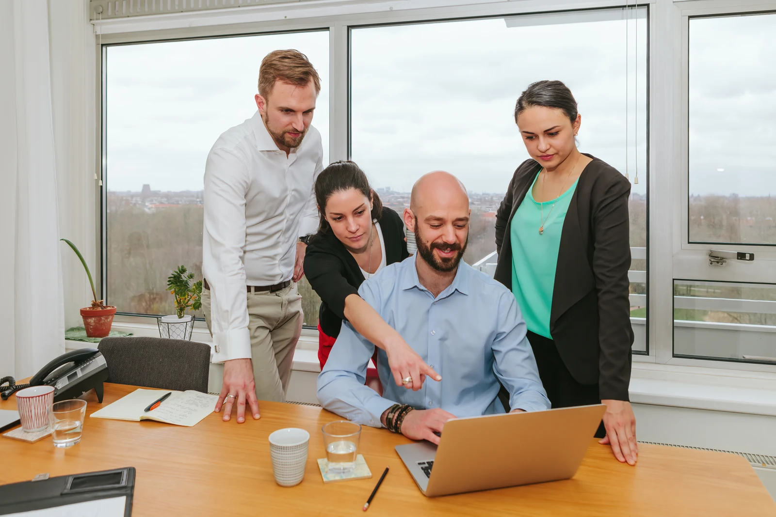 Four colleagues reviewing work together around a laptop in a bright office