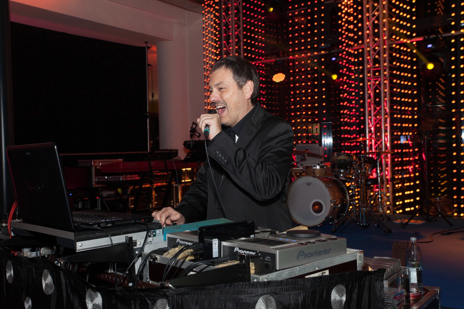 DJ hinter Mischpult mit Mikrofon in der Hand. Professionelle Moderation mit Stimmung. Stehend auf der Bühne mit toller Lichttechnik im Hintergrund