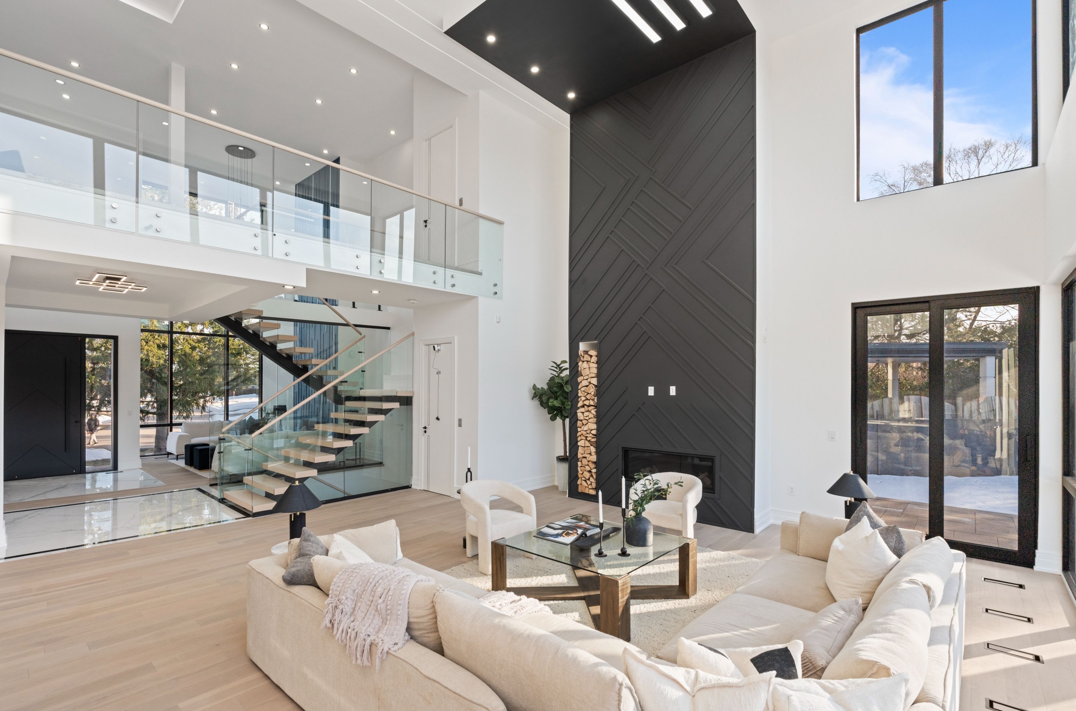 Modern living room with abstract art, beige sectional sofa, indoor plants, and large windows.