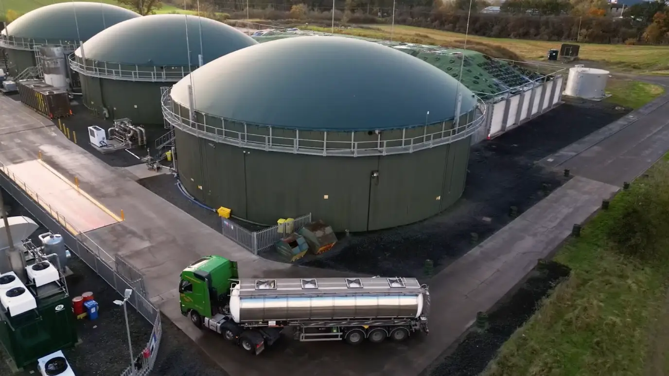 Aerial view of three large, rounded storage tanks next to a truck in a green landscape.