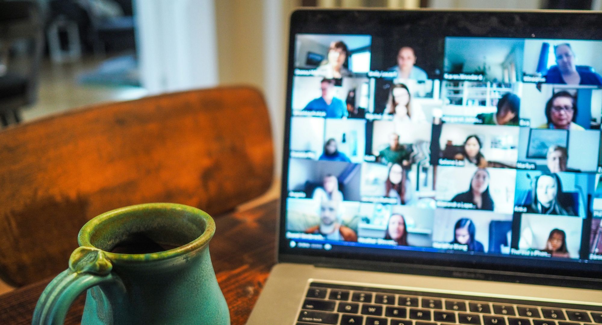 notebook com variás pessoas na tela em uma reunião e uma xícara de café ao lado