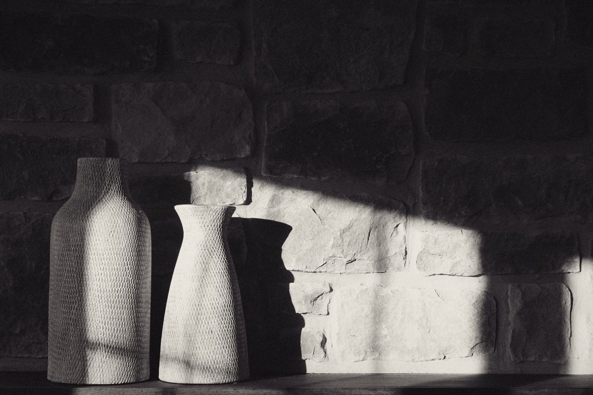 Two ceramic vases against a sunlit stone wall
