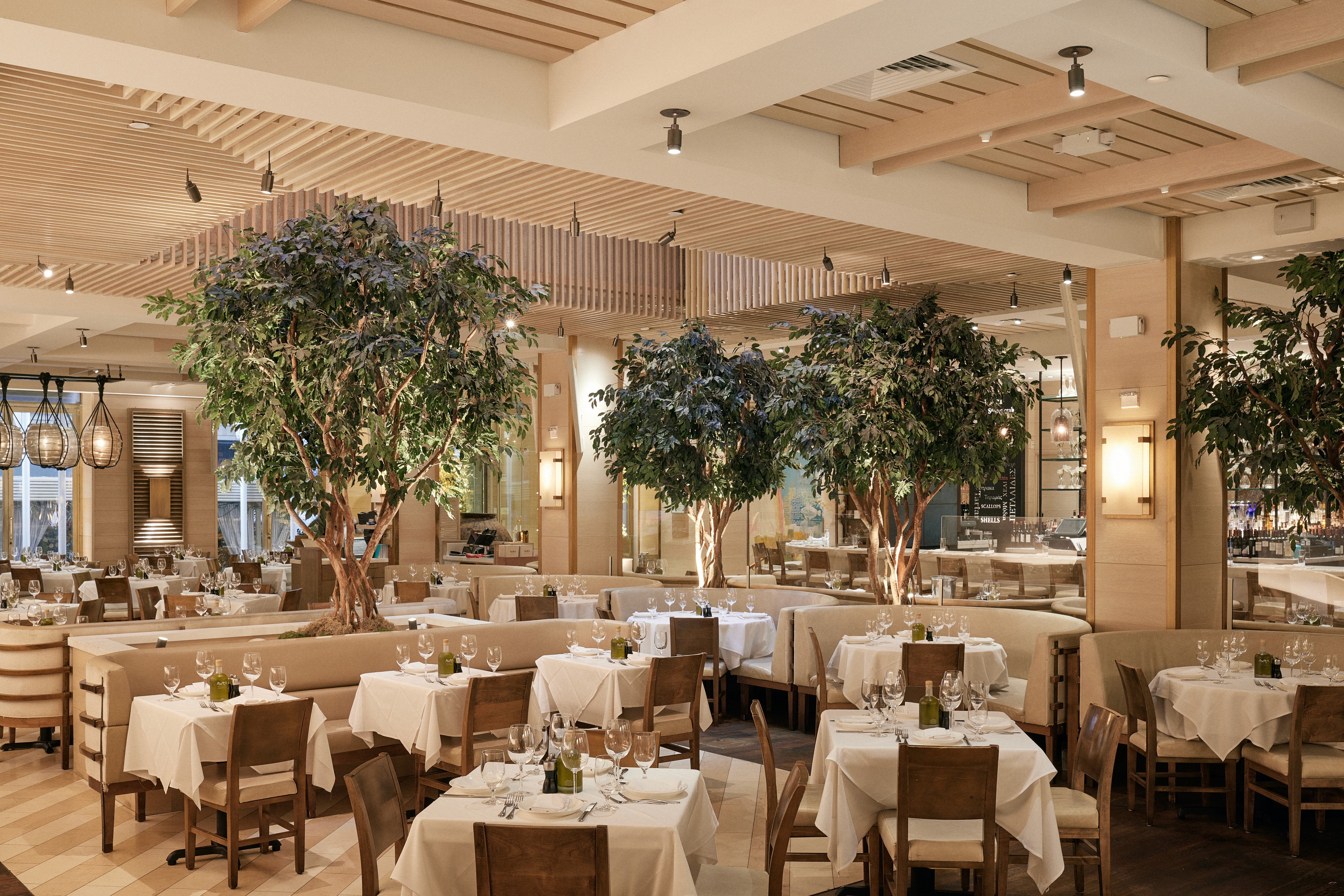 Interior of a stylish restaurant featuring indoor plants, elegant decor, and numerous dining tables with patrons.
