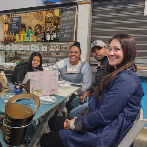 Four people sitting at a table in a casual dining setting, smiling at the camera, with drinks and menus on the table.