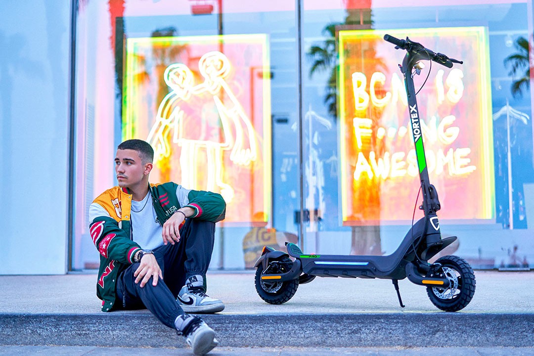 Jeune homme assis près d’une trottinette électrique ETRIC Vortex stationnée devant une vitrine urbaine colorée