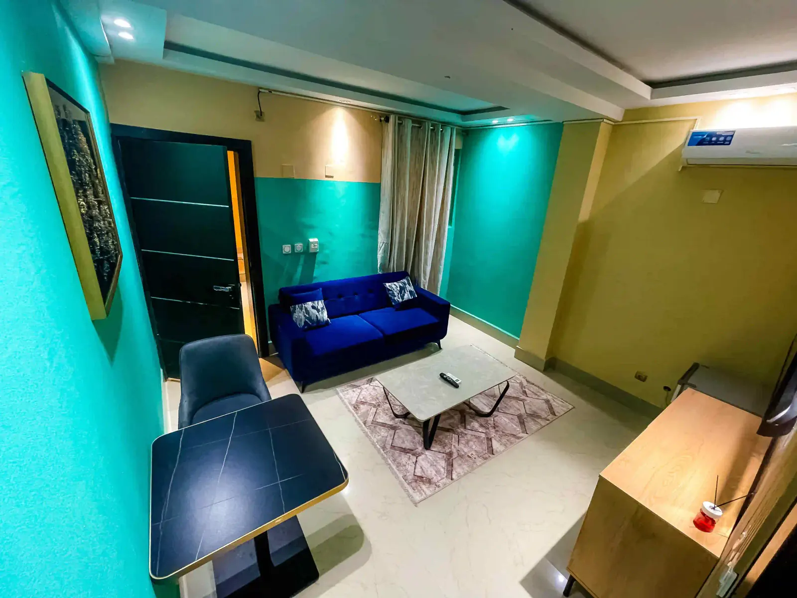 Vue du salon turquoise avec canapé bleu, table basse et télévision murale.