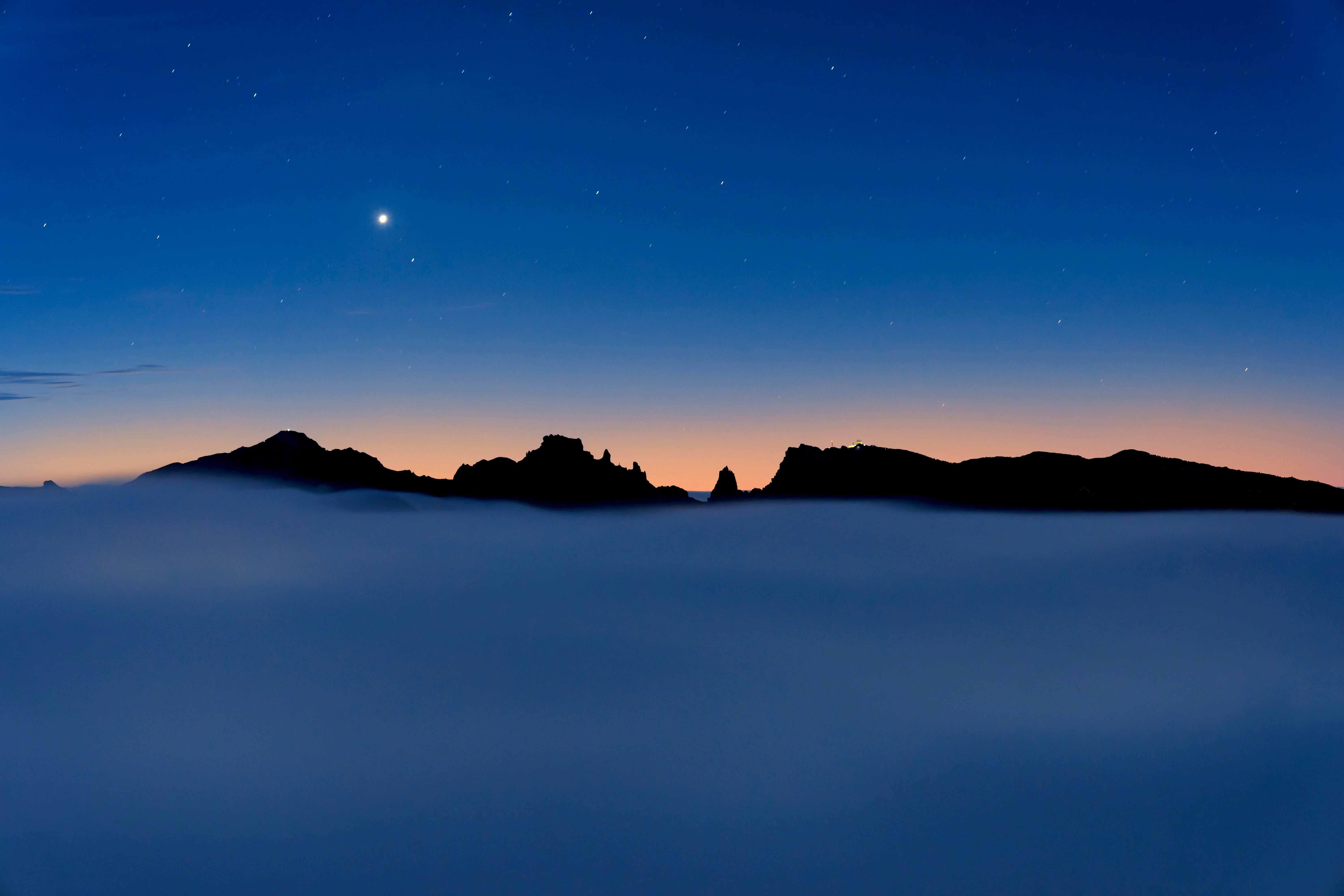 Mountain peaks emerge from clouds at twilight