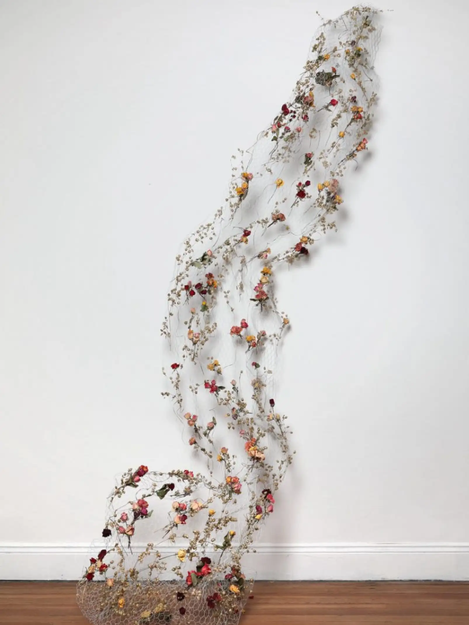 Escultura vertical de flores secas sobre malla metálica para instalación artística que evoca movimiento y ligereza.