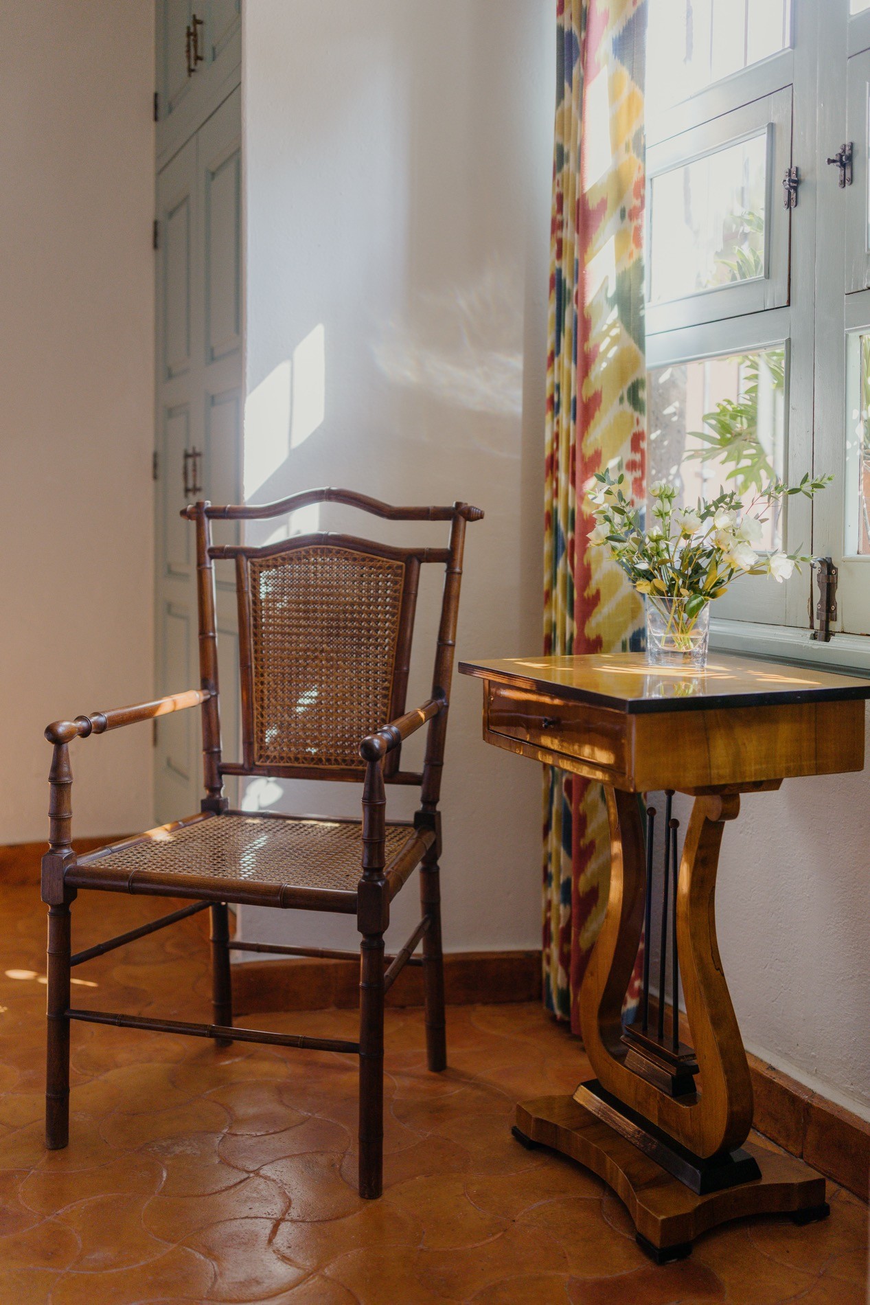 La Residencia bedroom detail with vintage cane chair, lyre table, and fresh flowers
