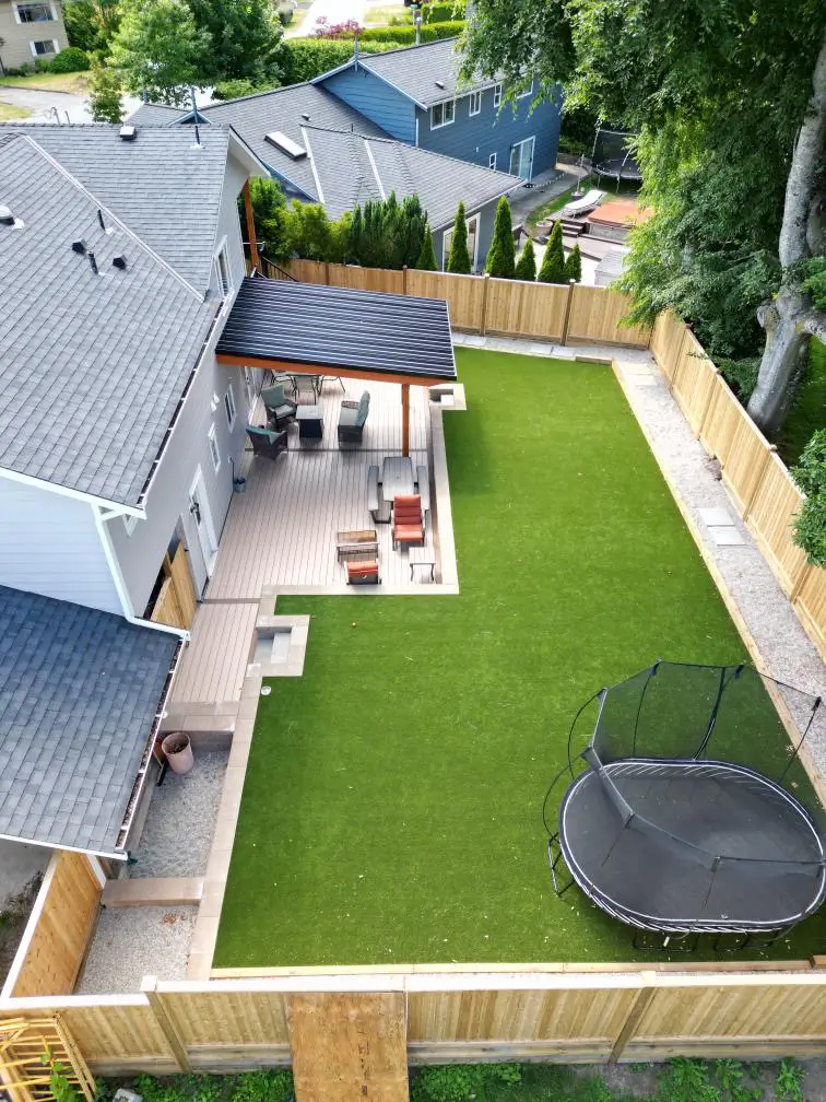 Landscaped backyard with artificial turf lawn, modern patio, and glass privacy fencing.