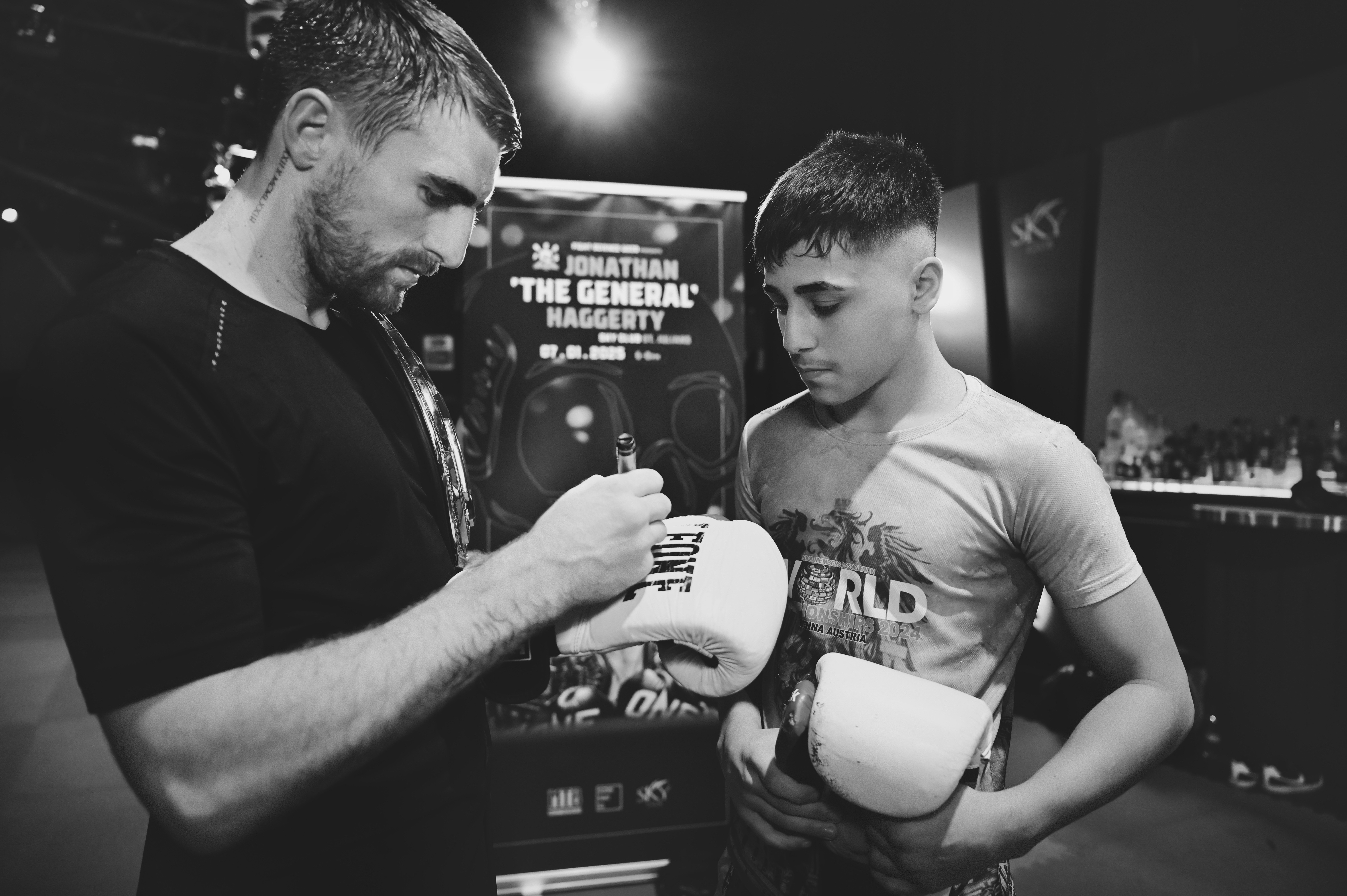 Two men talking beside a boxing ring at a live event, black and white