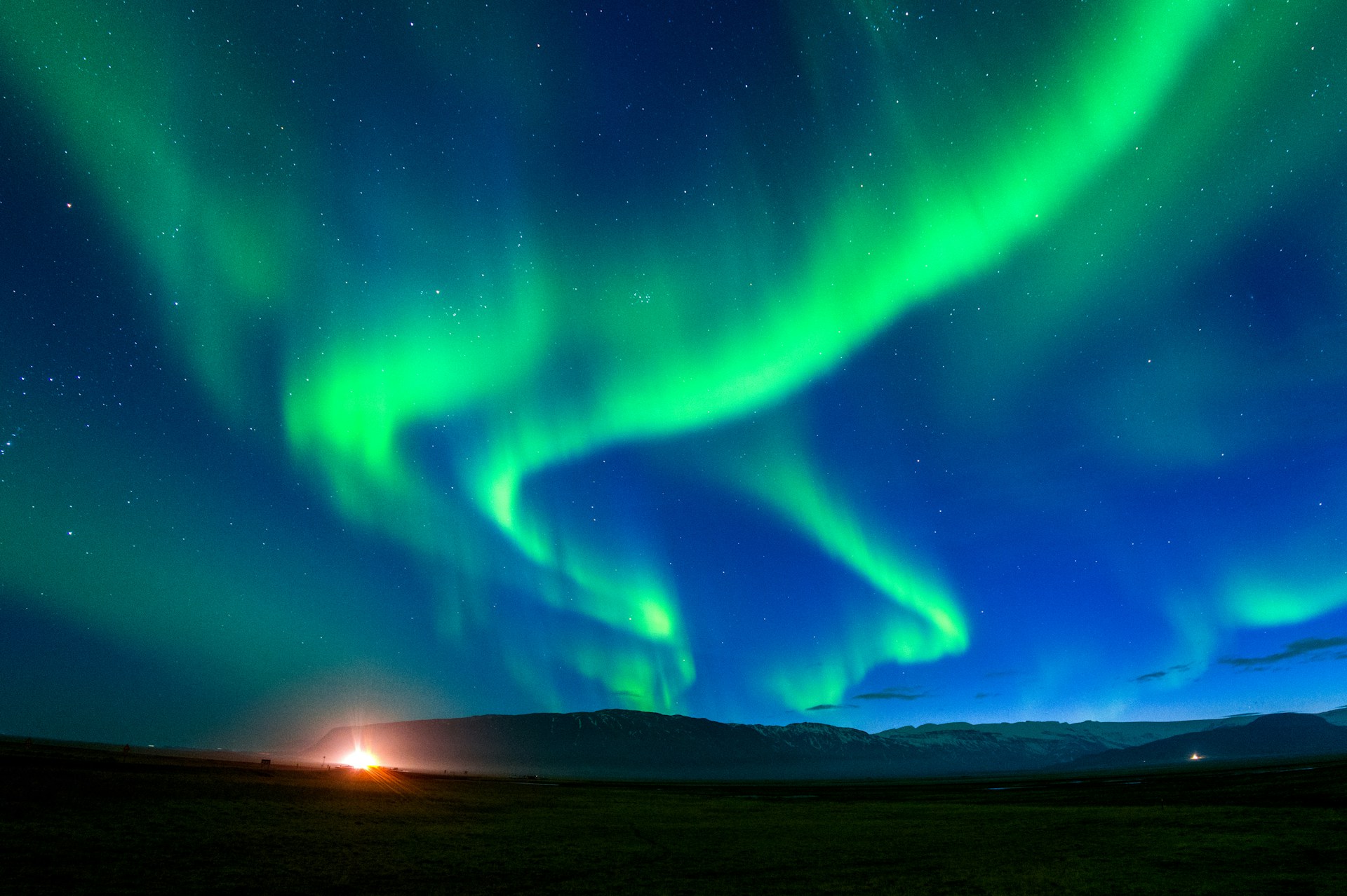 Bright green northern lights dancing across the night sky over the Icelandic countryside.