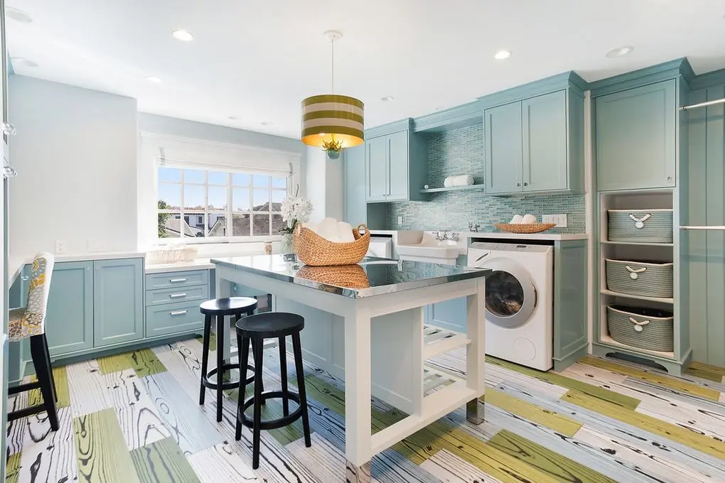 'Port Streets Remodel' vibrant laundry room with blue cabinetry, wicker basket on island, and lively patterned floor.
