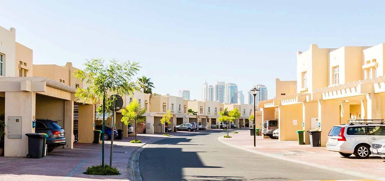 A street in Dubai featuring parked cars in front of Hattan 1 buildings under a clear blue sky.