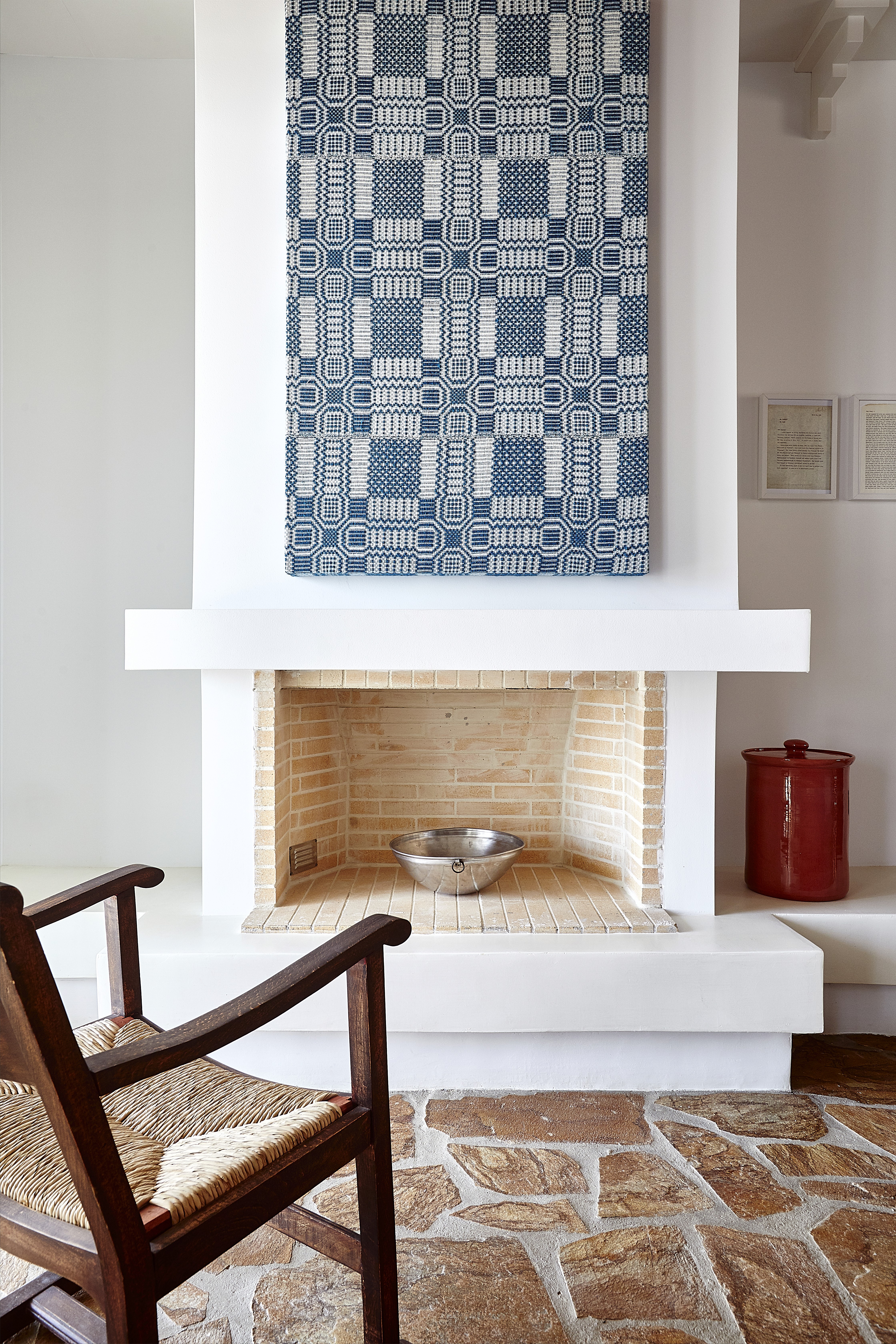 A chair in front of a fireplace with a blue artwork above