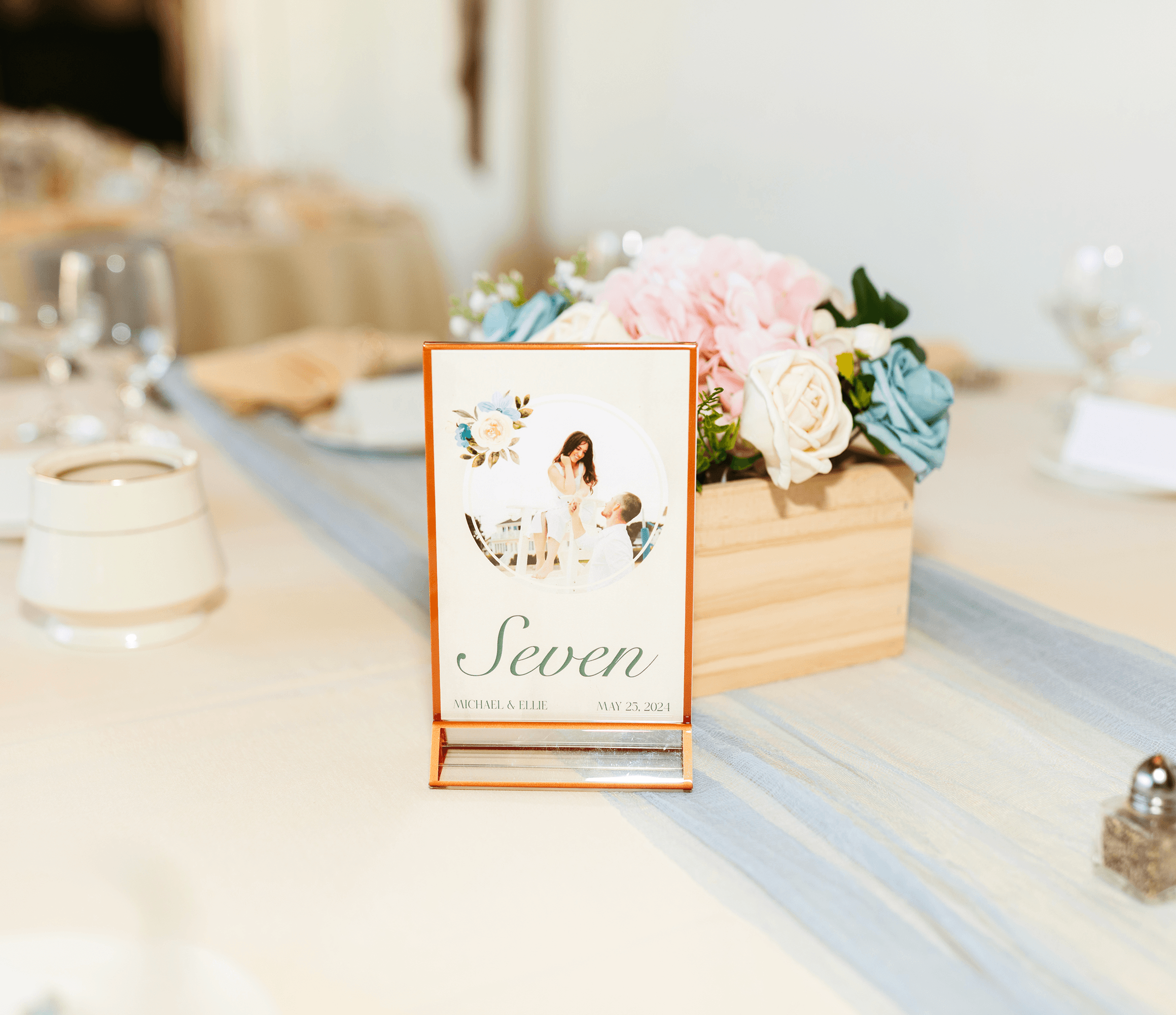 Photo of a wedding table sign designed in an elegat style with painted roses and an elegant serif typography. Designed by Will Lefkovich