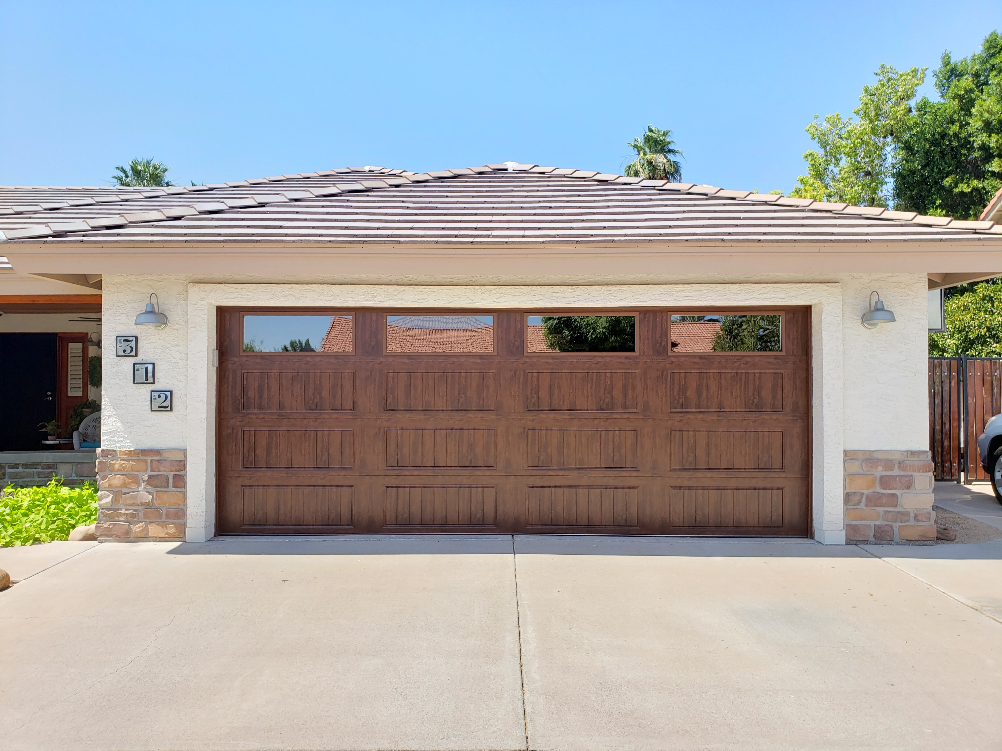 Driveway view of a synthetic wood garage door with glass windows along the top