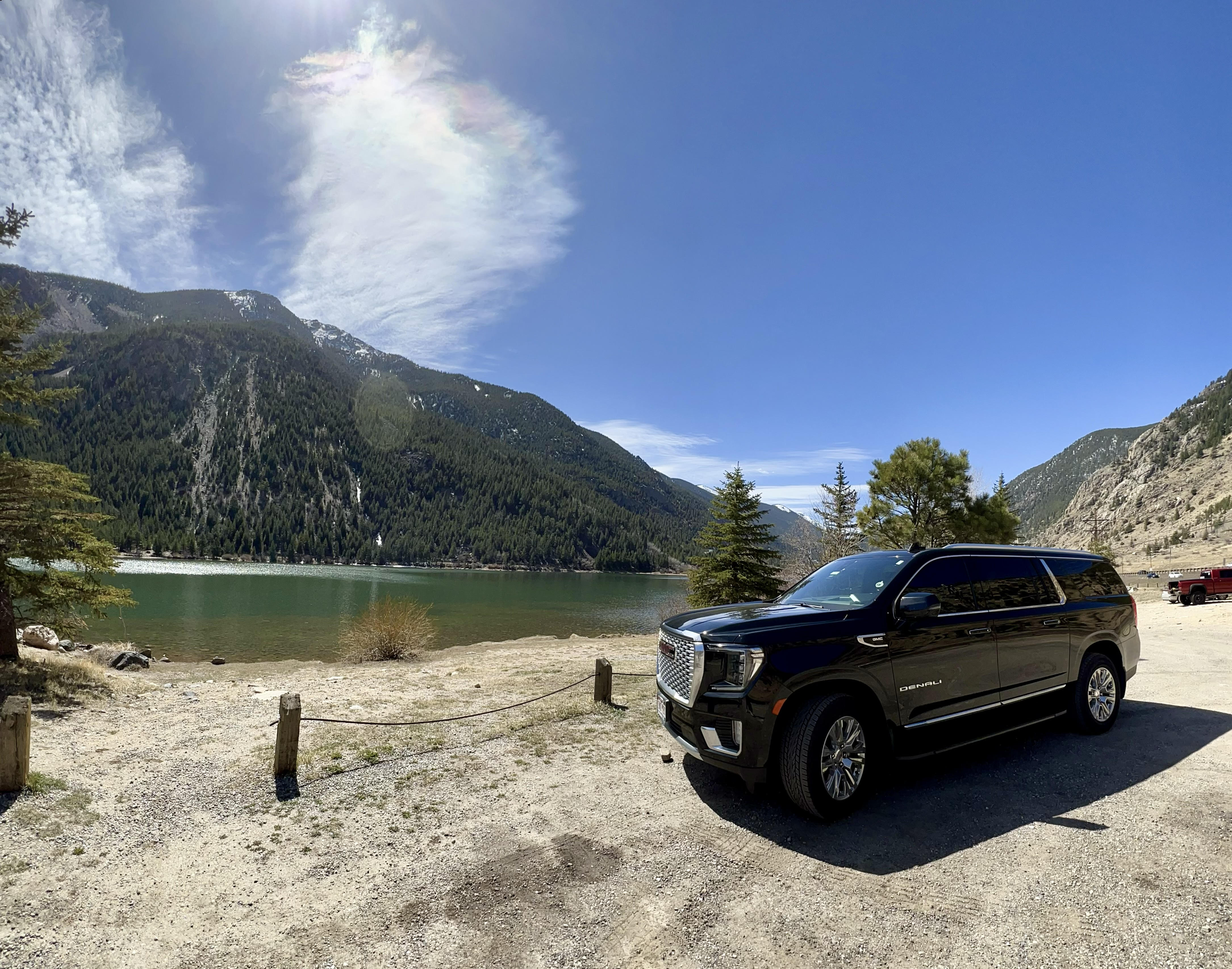 Avo Limo luxury black SUV parked beside a scenic Colorado mountain lake, surrounded by pine trees and snow-capped peaks under a clear blue sky—perfect for private limo service to the Colorado mountains.