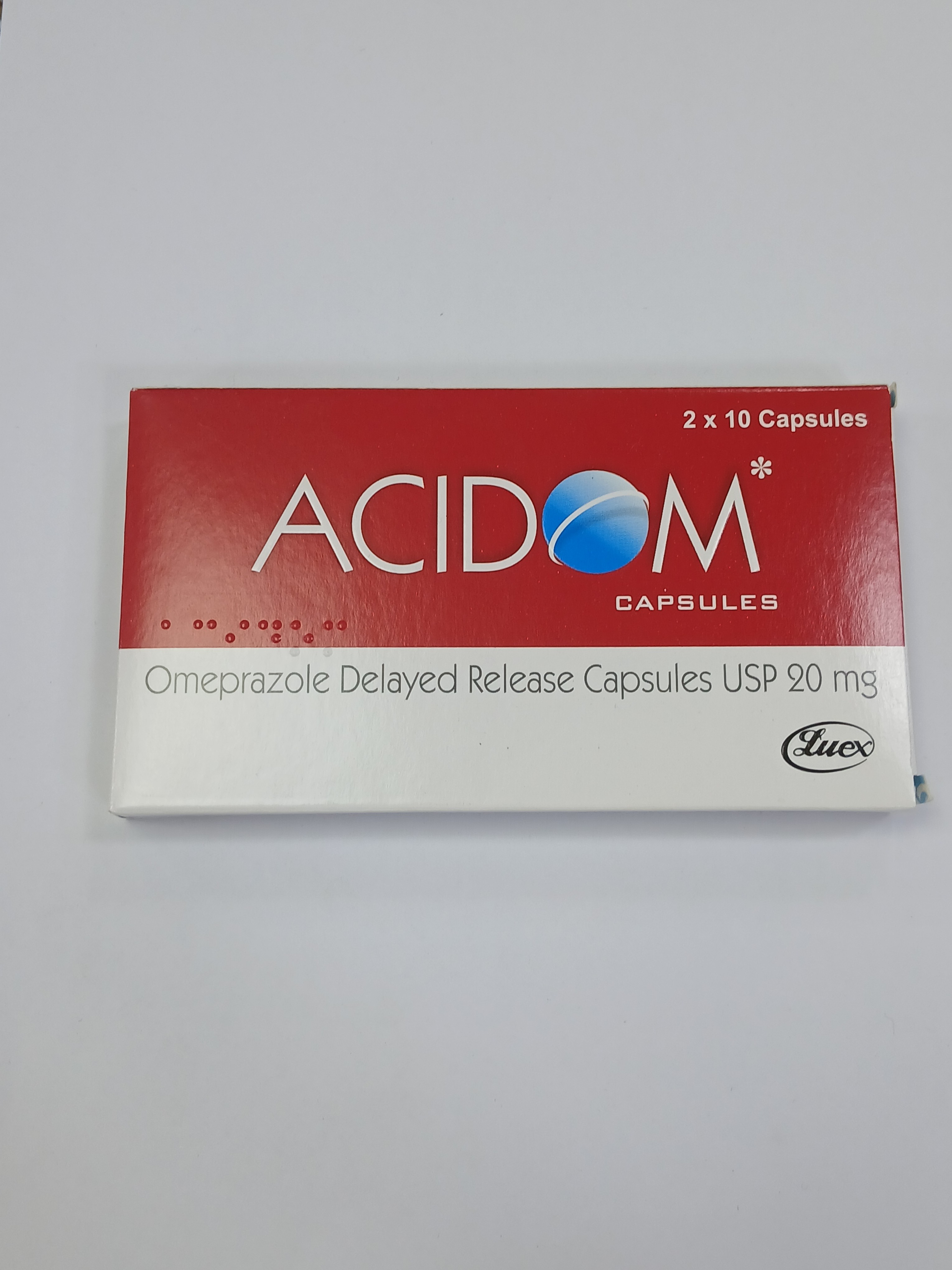 White and red cardboard packaging for delayed-release capsules displays printed text in blue and black, arranged in two rows of ten capsules each.
