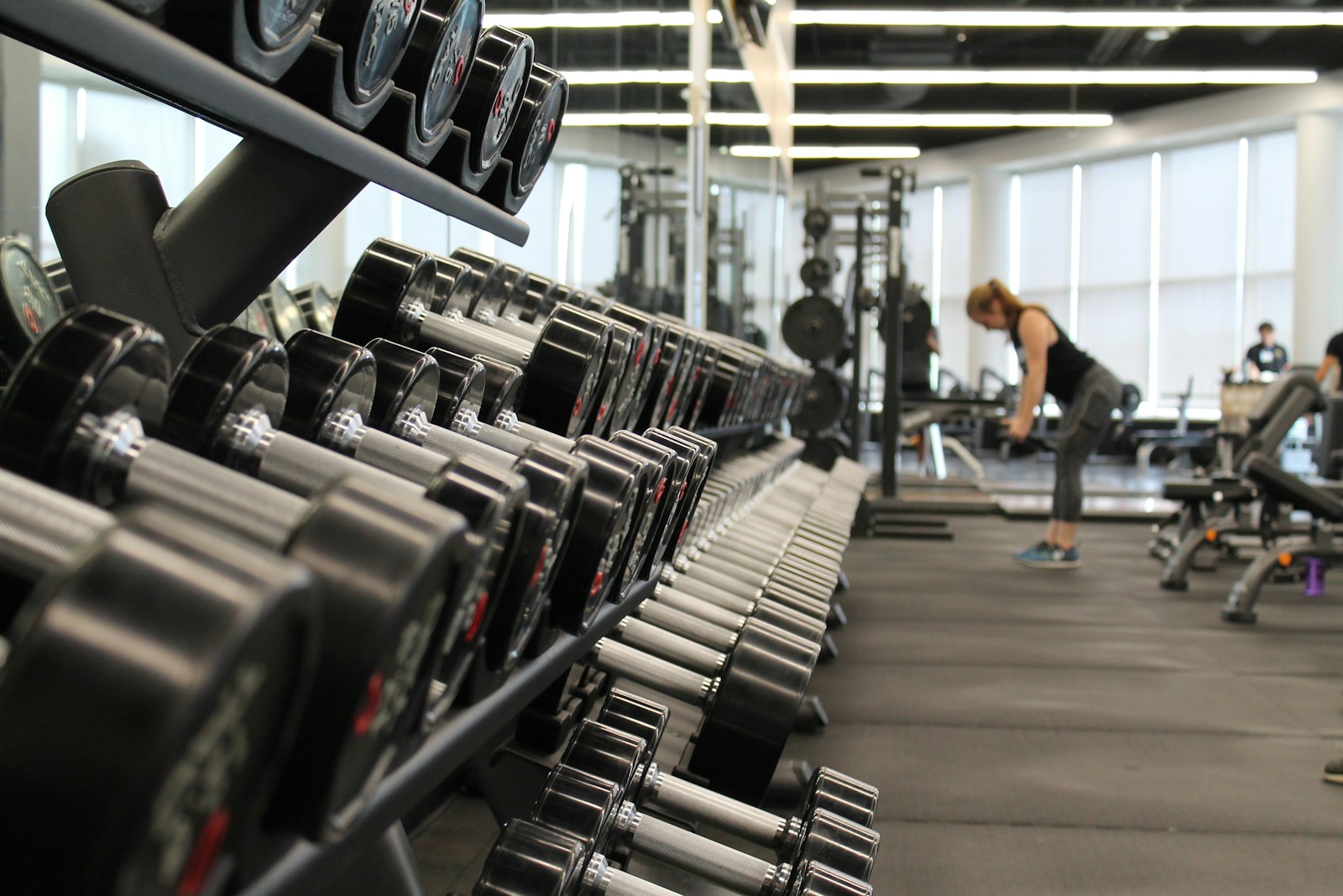 A woman standing among racks of dumbbells and exercise equipment in a gym, ready for resistance training.