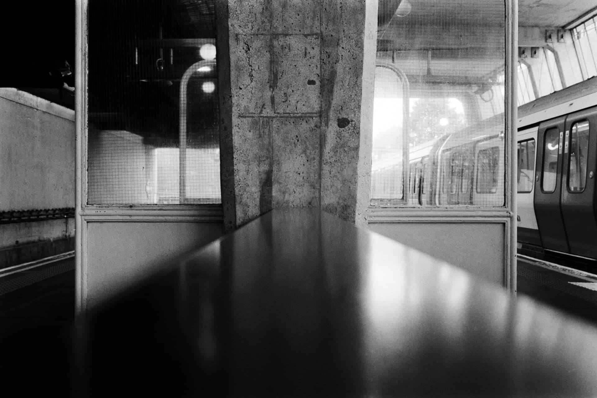 Concrete pillars and glass panels inside Uxbridge Underground station with train reflections