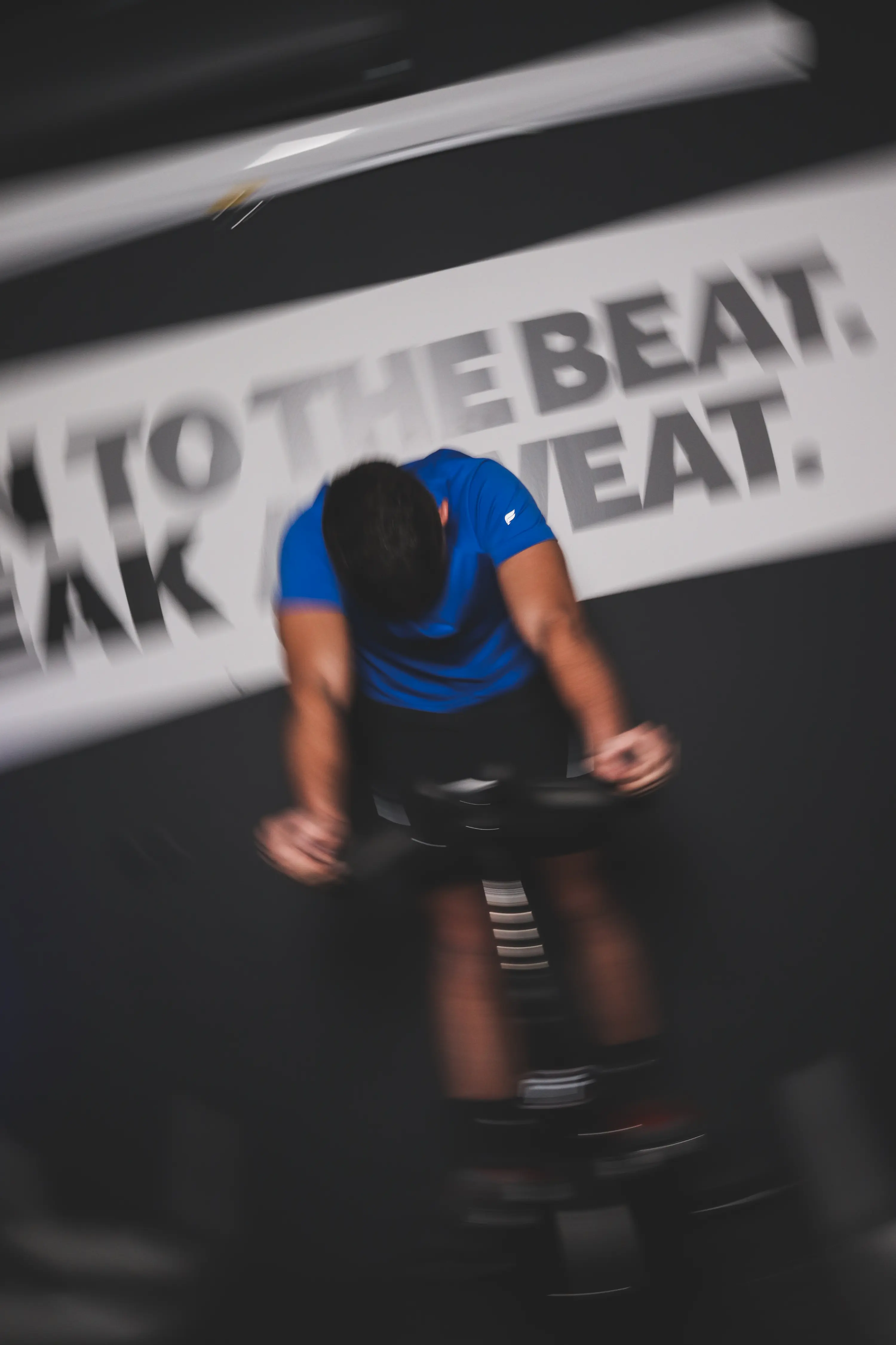 Participant en t-shirt bleu pédalant intensément sur un vélo de cycling avec effet de flou dynamique dans la spin room