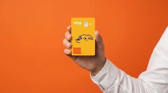 Mão segurando o cartão de benefícios amarelo da Caramelo, com o desenho de um cachorro caramelo e a bandeira Visa