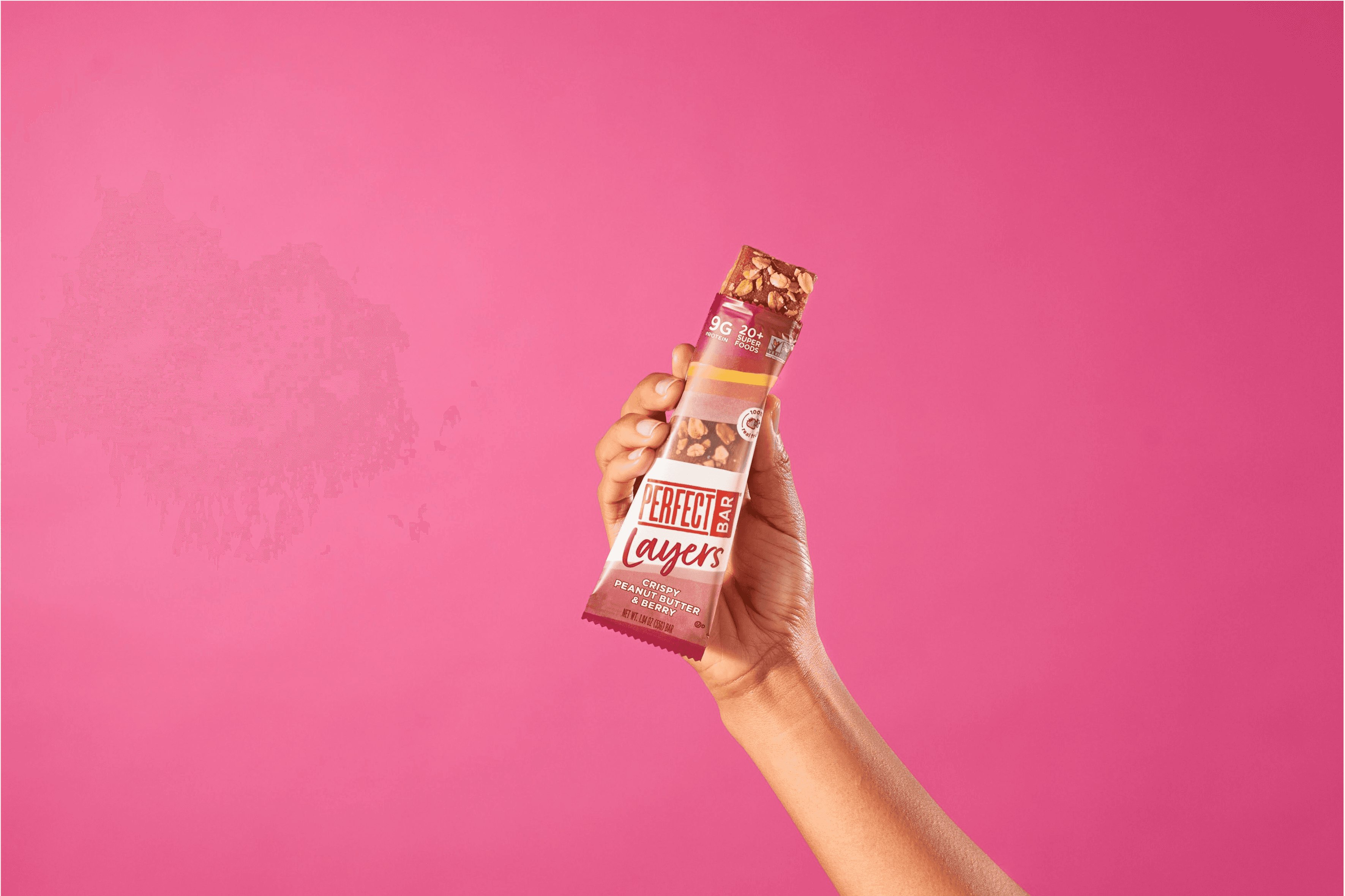 Hand holding a styled Crispy Peanut Butter & Berry Perfect Bar with top of package open and bar coming out of the top.