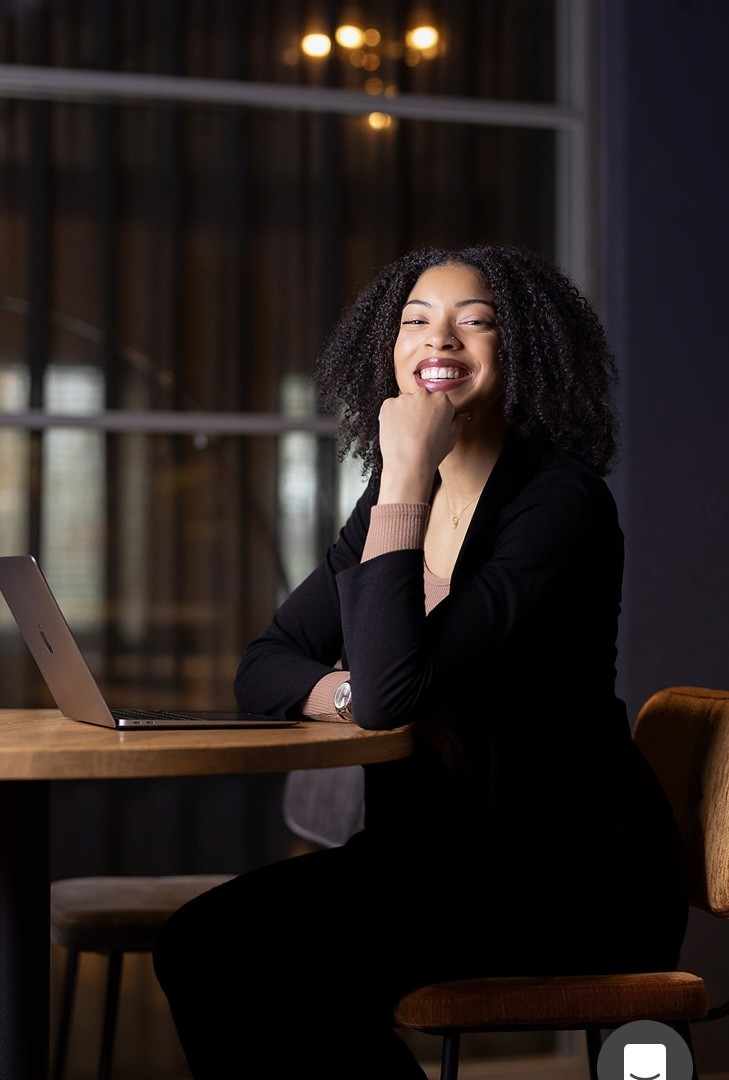 A woman lying down on a soft surface with her eyes closed, bathed in warm sunlight filtering through leaves. Her face has a natural glow, reflecting relaxation and tranquility in a serene spa-like setting.