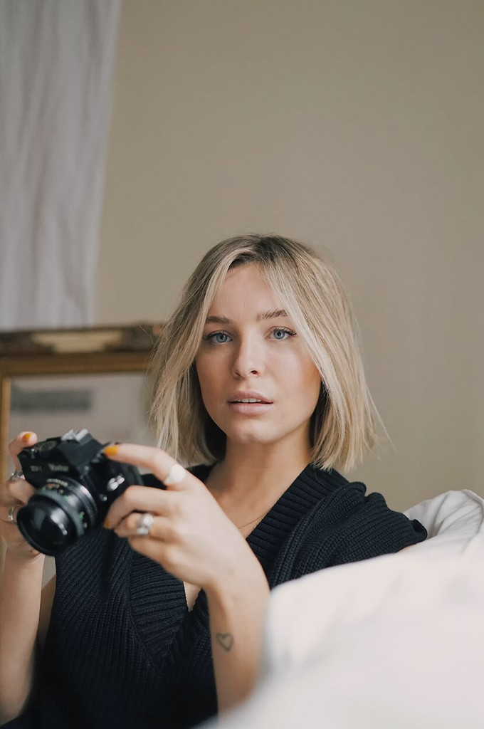 A person with short blonde hair holds a vintage camera.