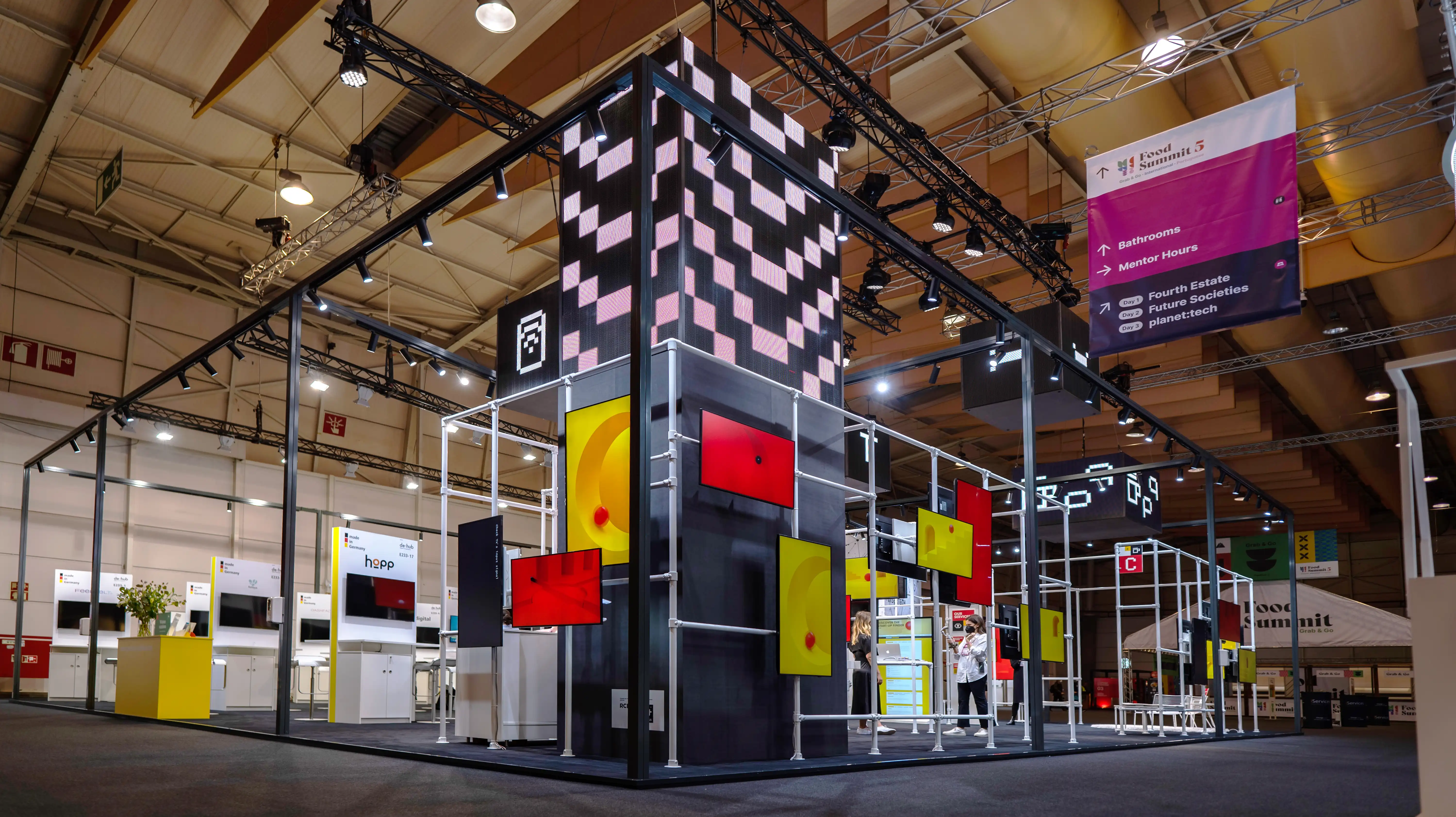 Trade fair booth of the German Pavilion with checkered tower, truss lighting frame and colorful panels at Web Summit in Lisbon.