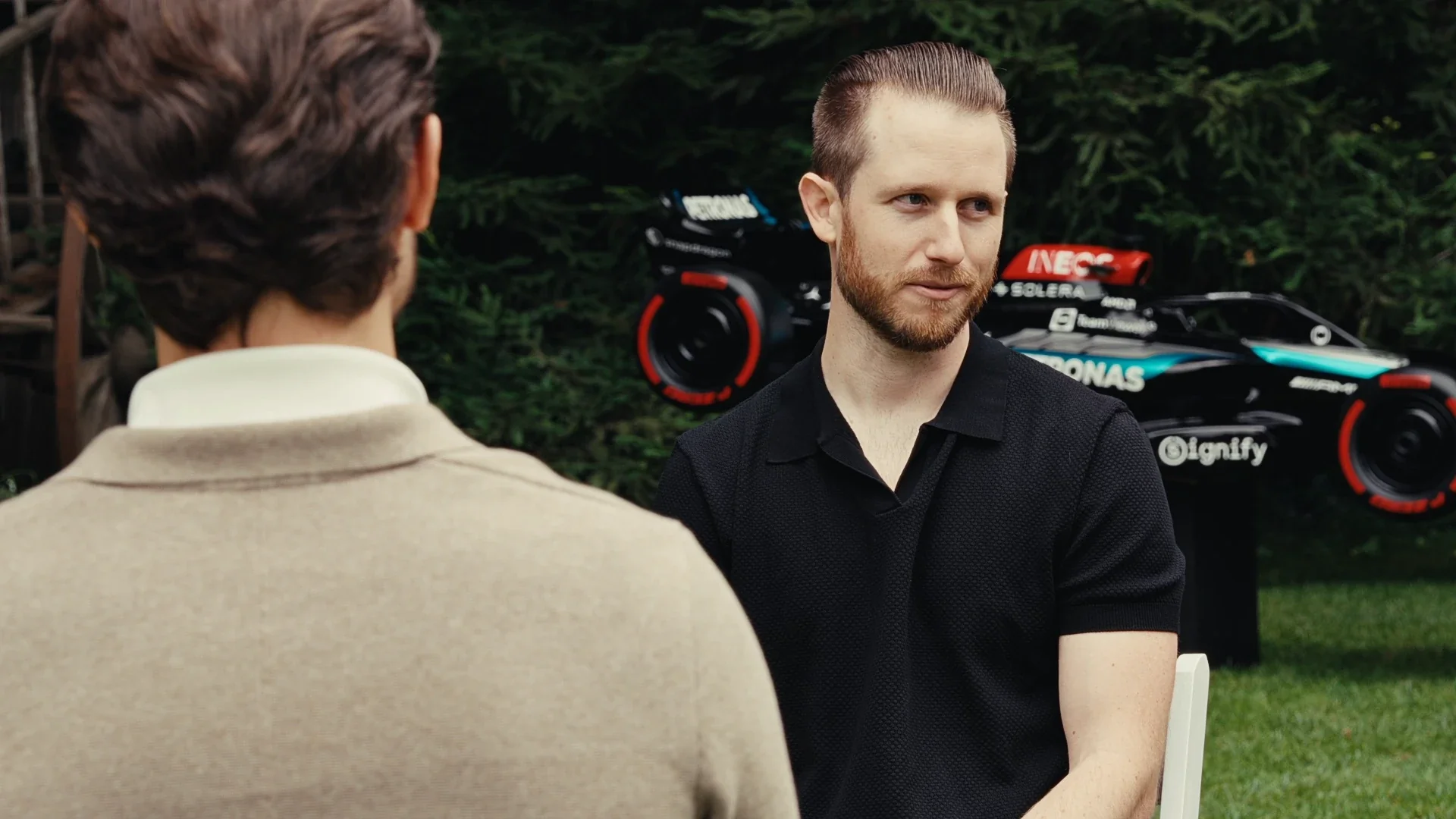 Two men talking in front of a race car