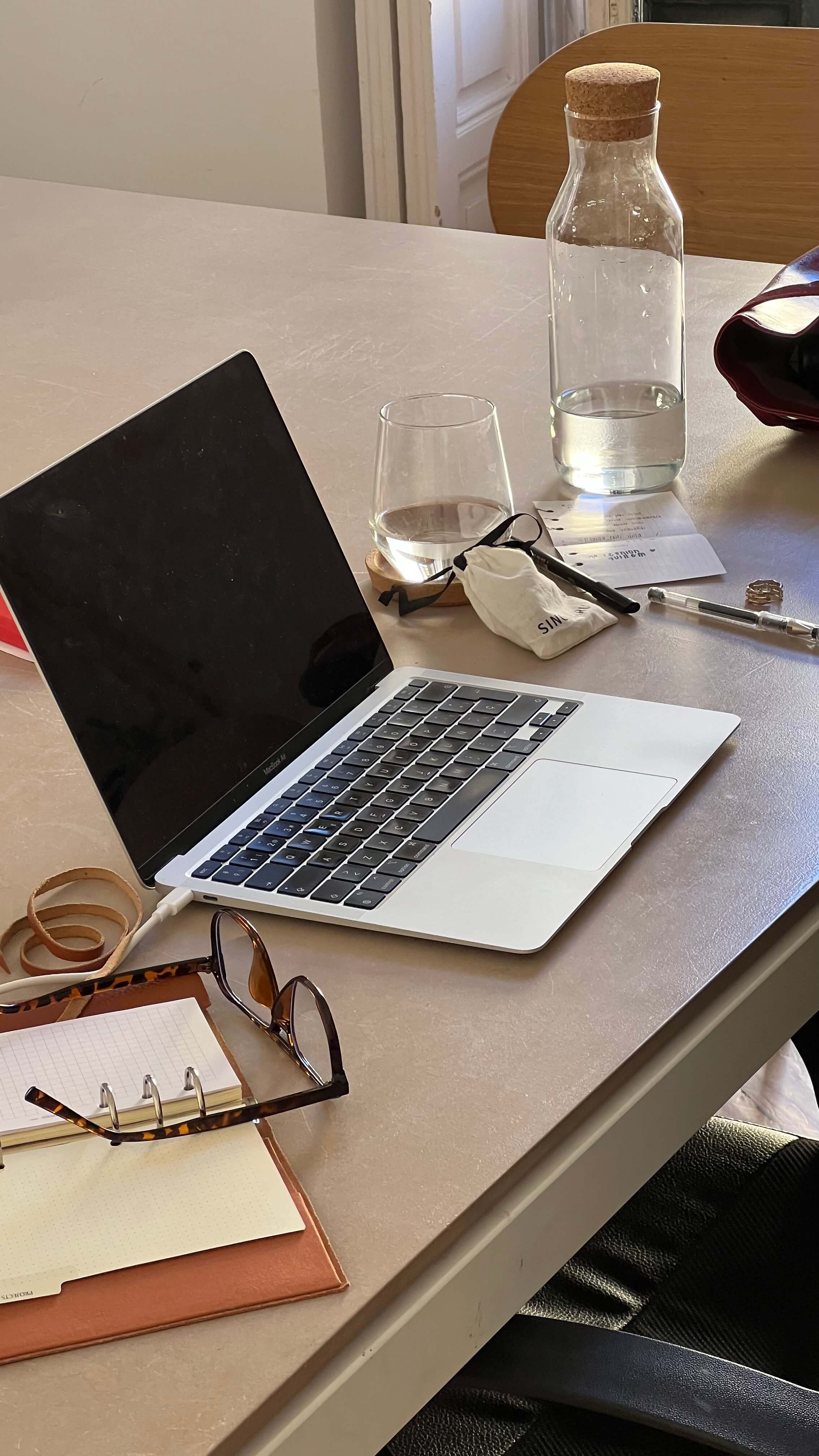 a desk with a water bottle, open laptop, planner, and reading glasses